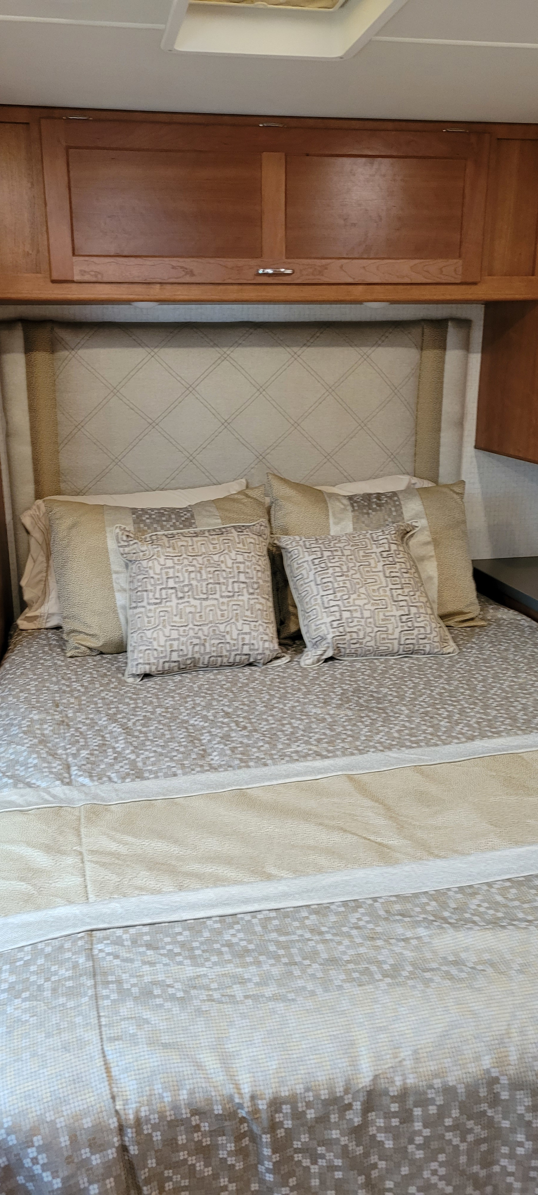 Inside an RV rental: a cozy bed with patterned headboard, neutral pillows/comforter, and overhead wooden cabinets.. Winnebago Minnie Winnie 2016