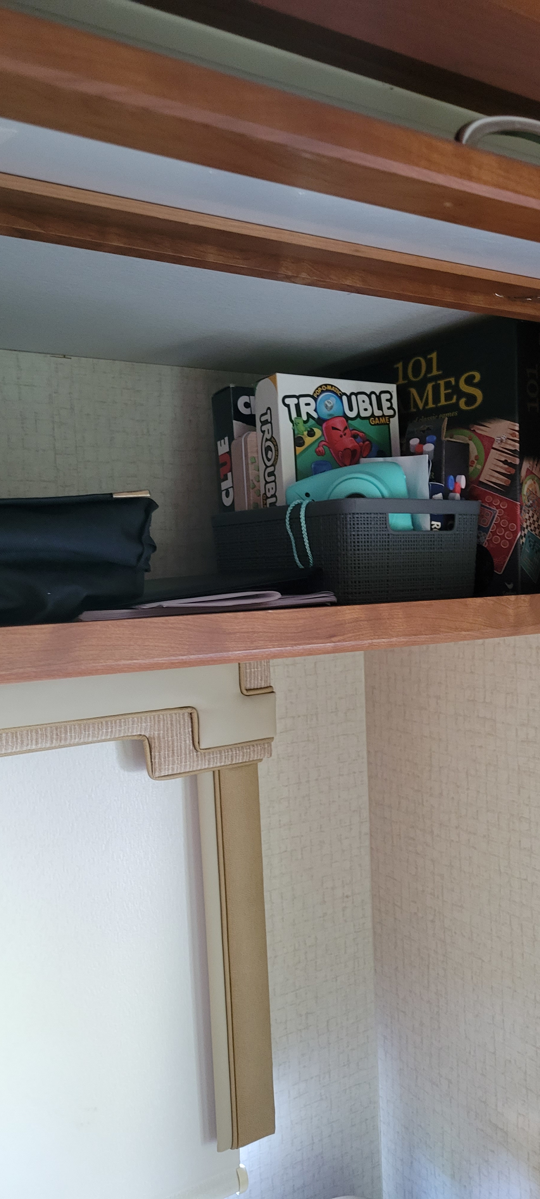 Organized RV rental shelf with board games (Trouble, Clue), a turquoise camera, and storage bins.. Winnebago Minnie Winnie 2016