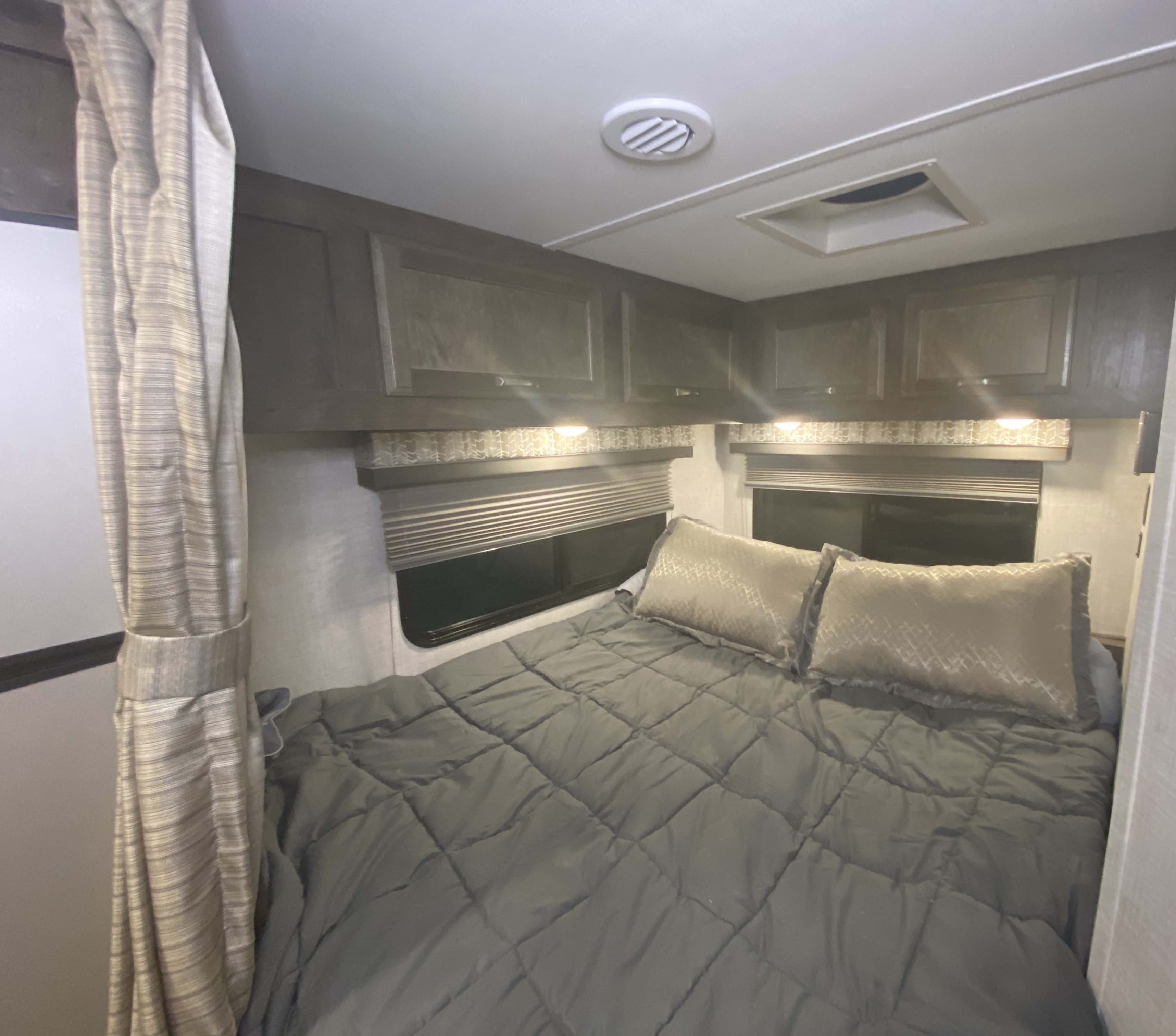 Cozy RV rental bedroom with a comfy bed, overhead storage cabinets, window blinds, and ceiling fixtures.. Gulf Stream Conquest 2022