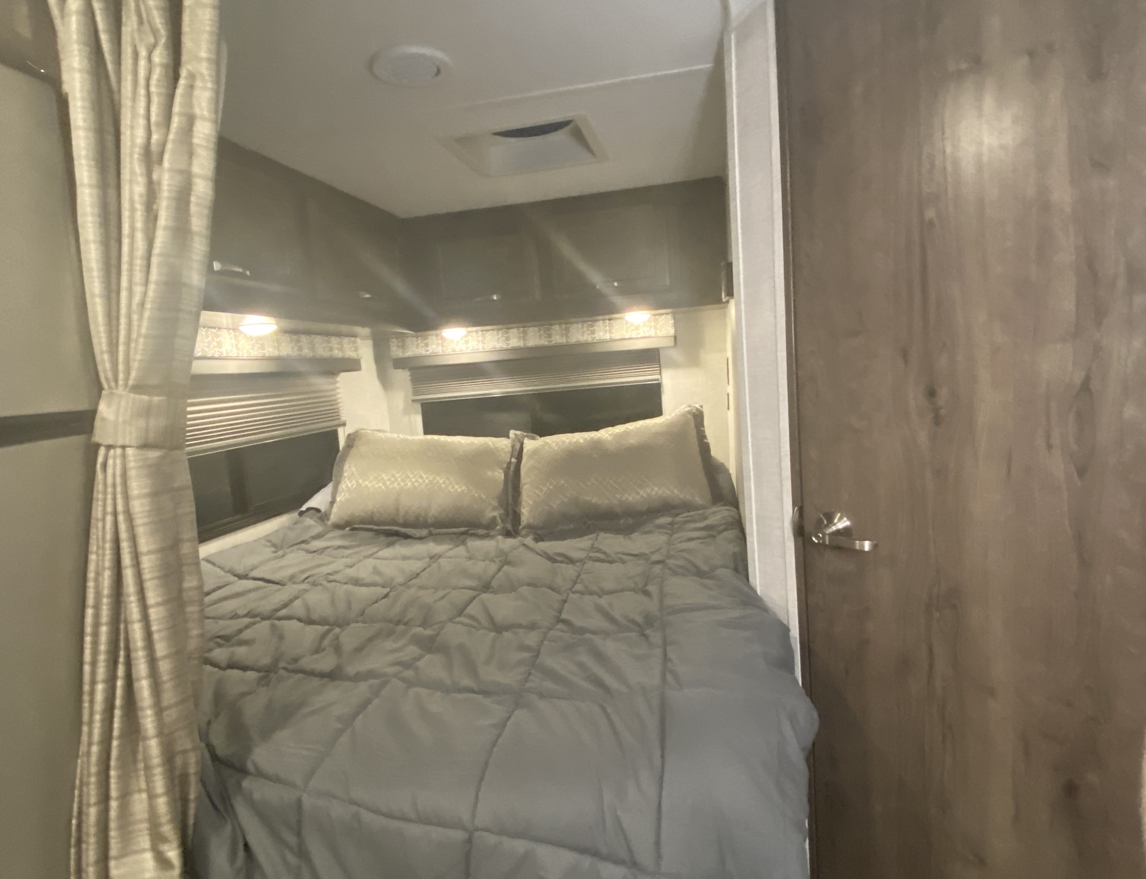 A comfortable RV rental bedroom with a gray bed, light pillows, windows with blinds, and overhead storage cabinets.. Gulf Stream Conquest 2022
