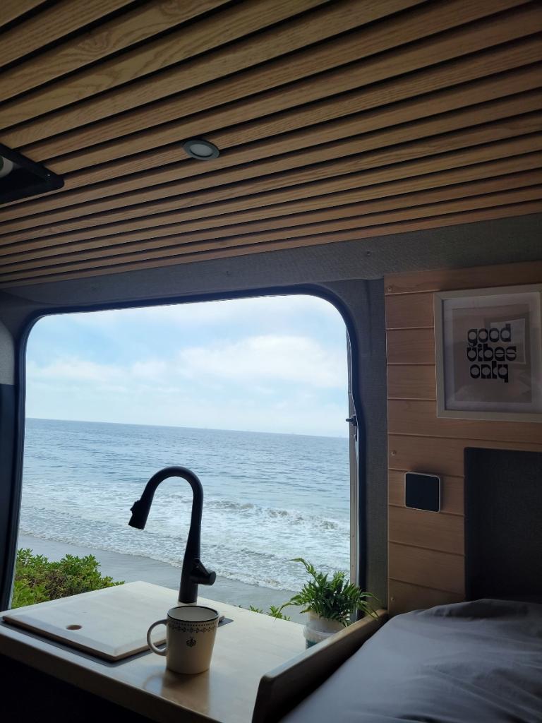 Scenic RV rental interior with ocean view, kitchenette, and bed. Perfect for a cozy beach getaway.. Mercedes-Benz Sprinter 2021