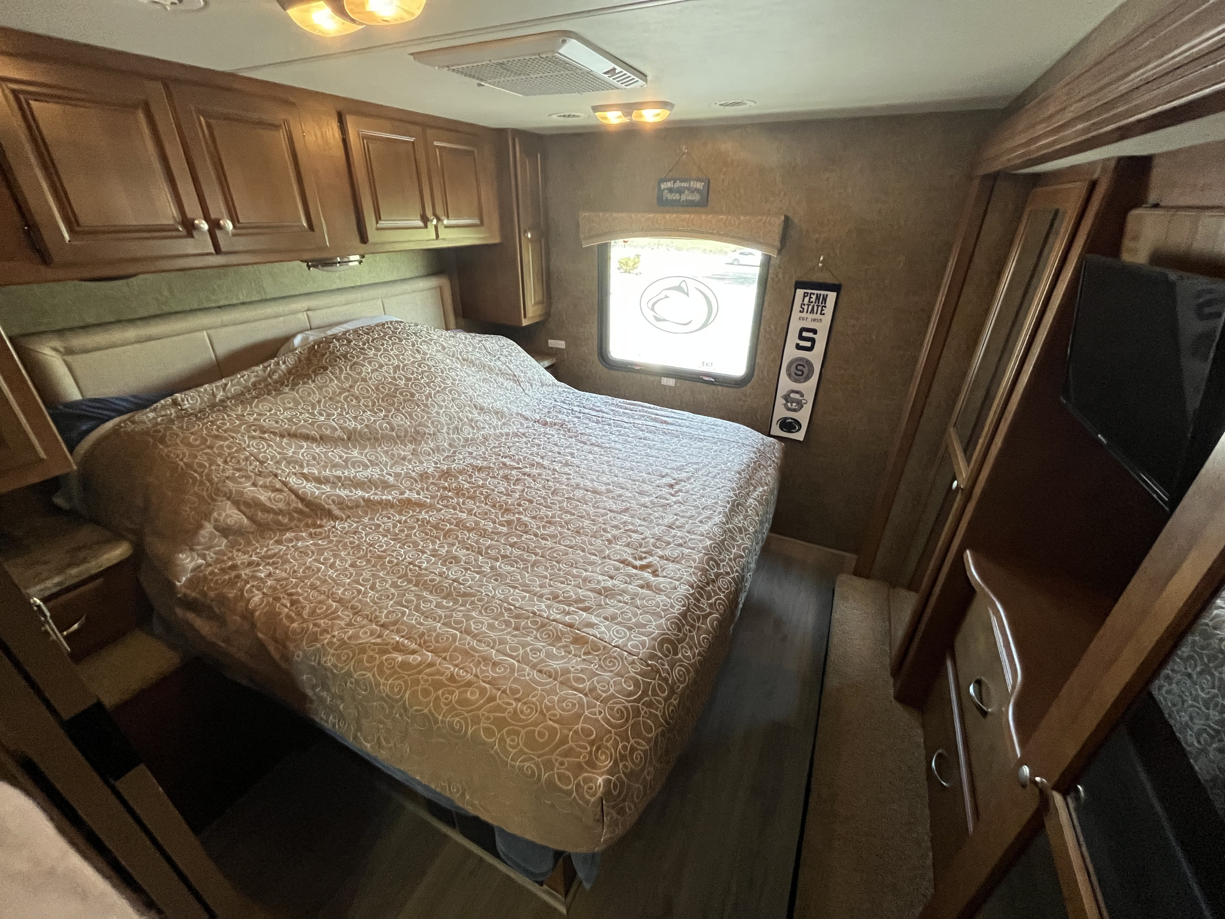 RV rental bedroom showcasing a patterned bed, wood cabinets, and Penn State details. A compact, comfortable space.. Other Miramar 2014