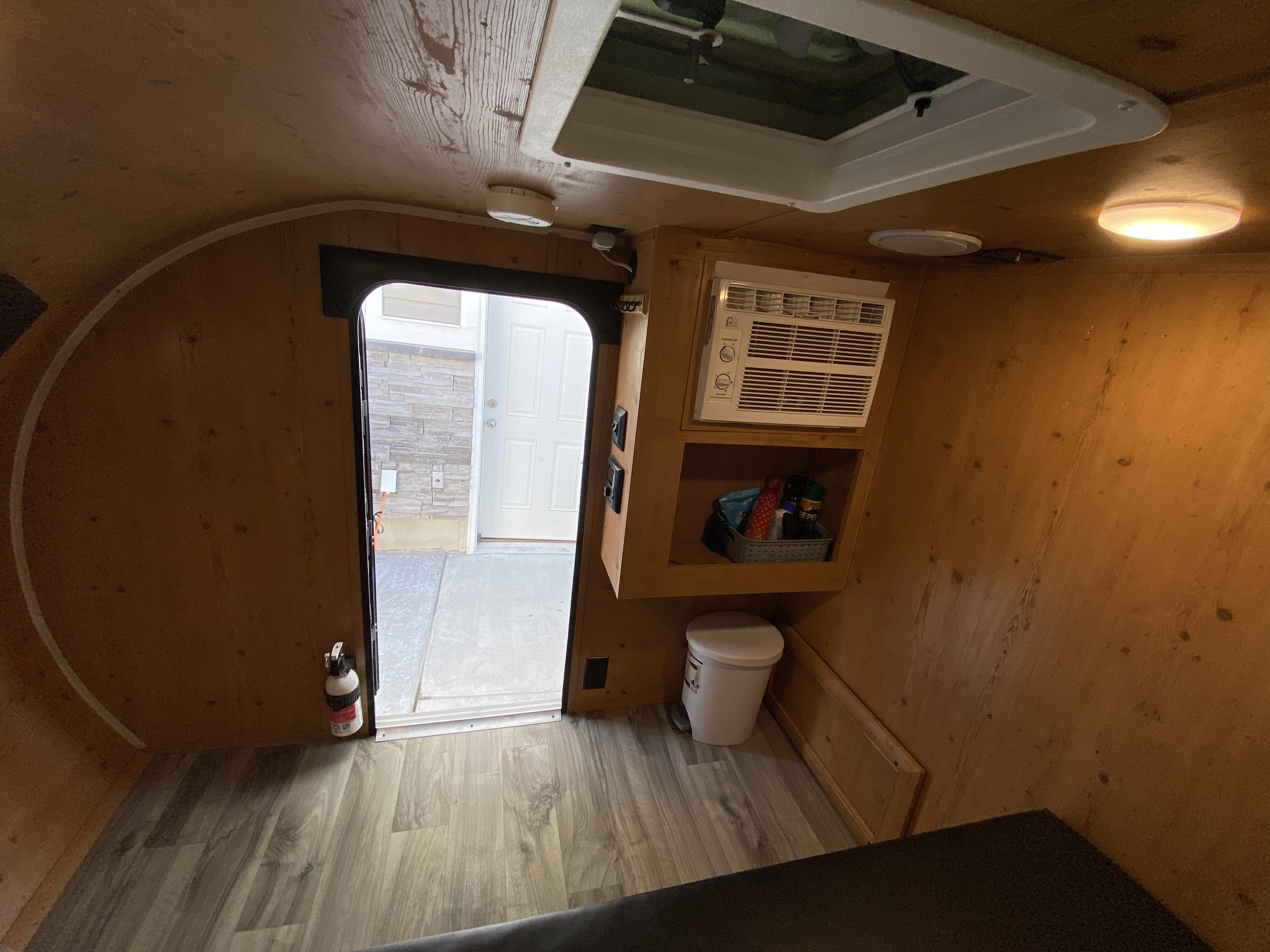 Inside a cozy **rv rental**: wood-paneled walls, AC unit, vinyl floor, and open door. Perfect compact camper setup.. Sunset Park RV SunRay 2020