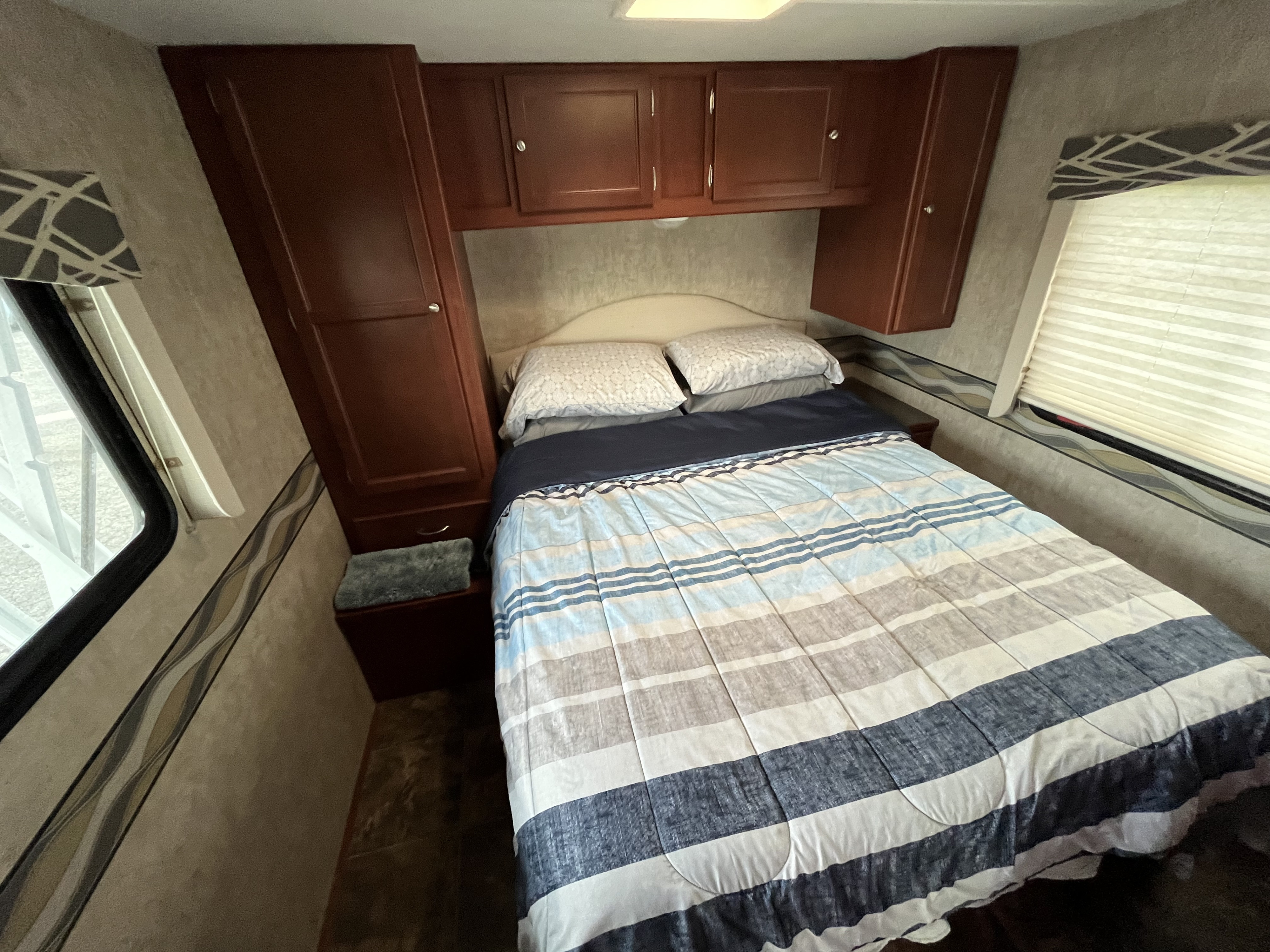 RV rental bedroom features a comfortable bed with striped bedding, dark wood cabinets, and windows for natural light.. Itasca Spirit 2014
