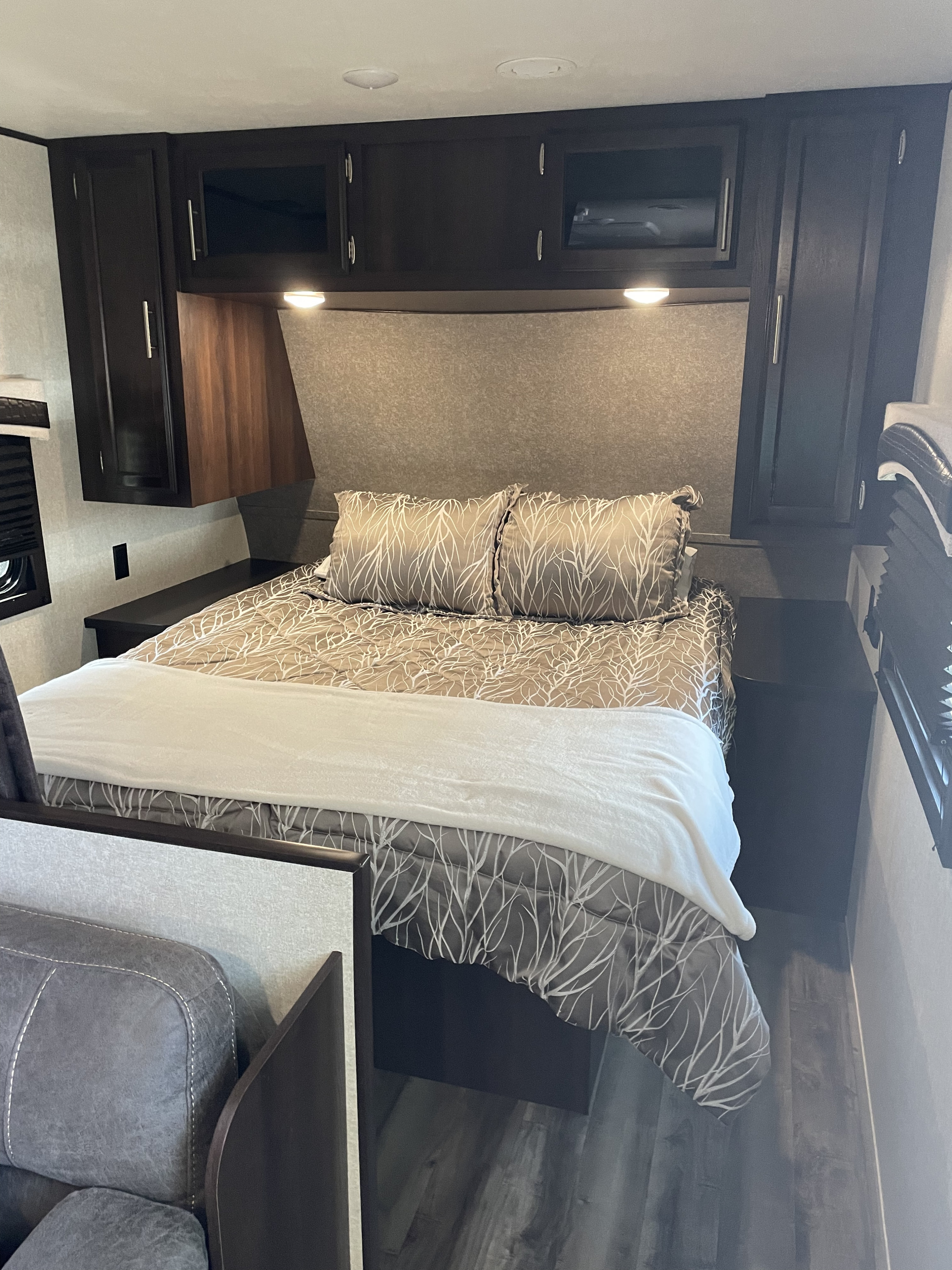 Inside an **RV rental**: a modern bedroom with patterned bedding, dark wood cabinets, and two nightstands.. Jayco Jay Flight 2020
