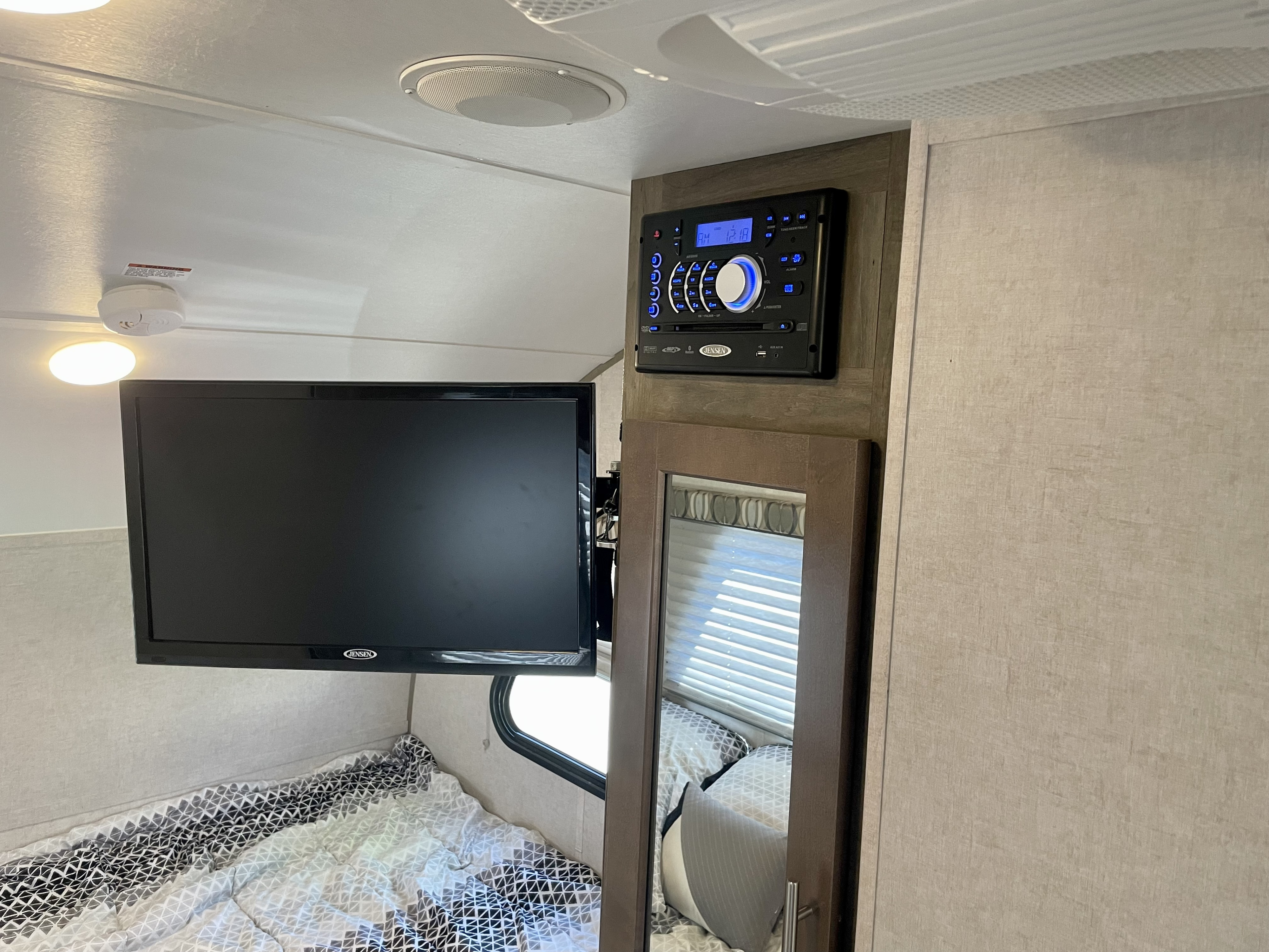 Inside an RV rental: Compact bedroom featuring a wall-mounted TV, Jensen entertainment system, and full-length mirror.. R-Pod Hood River Edition 2017