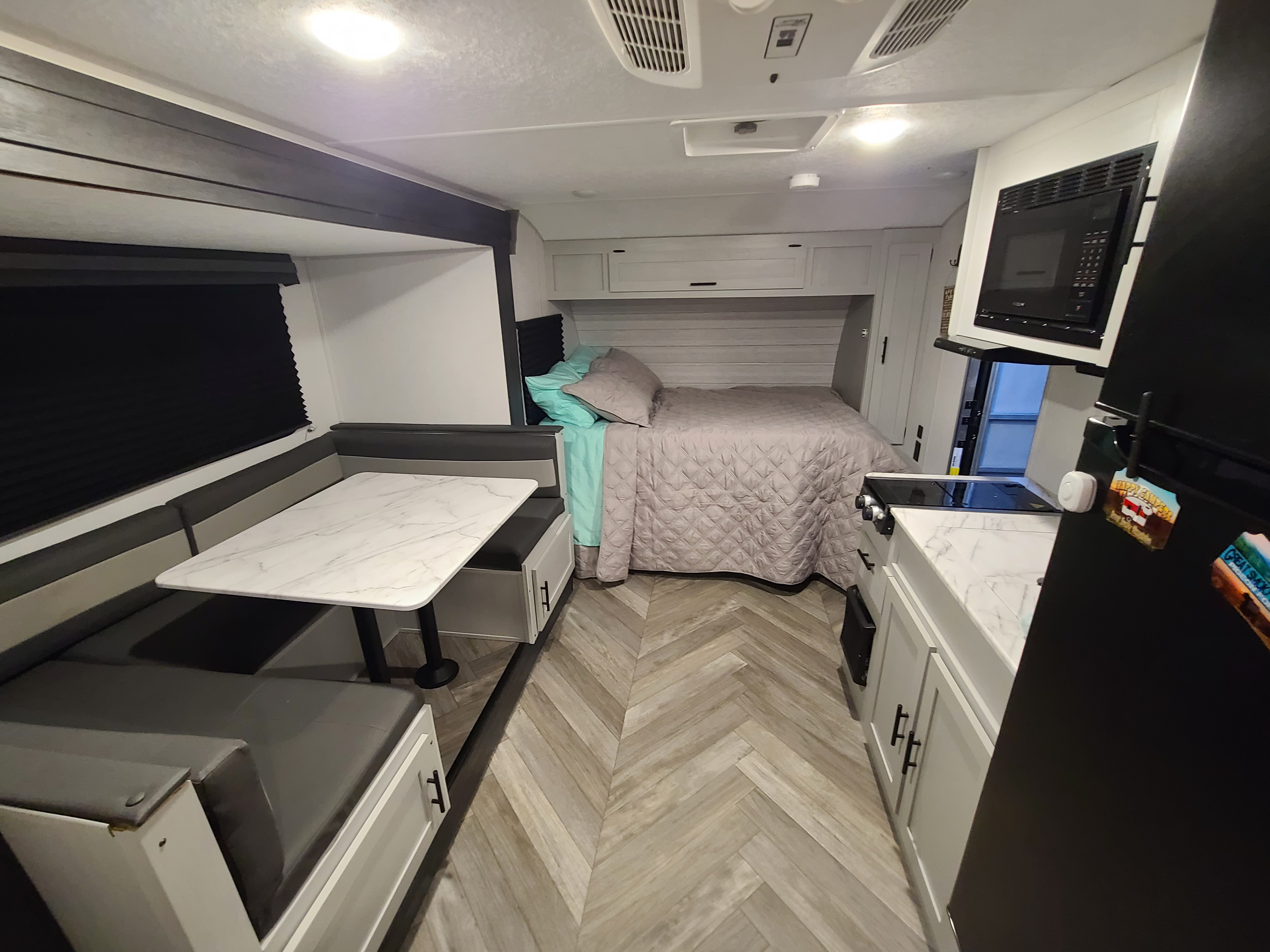 Modern rv rental interior featuring a dinette, cozy bed, and full kitchen with light wood floors.. Forest River Wildwood FSX Platinum 2021