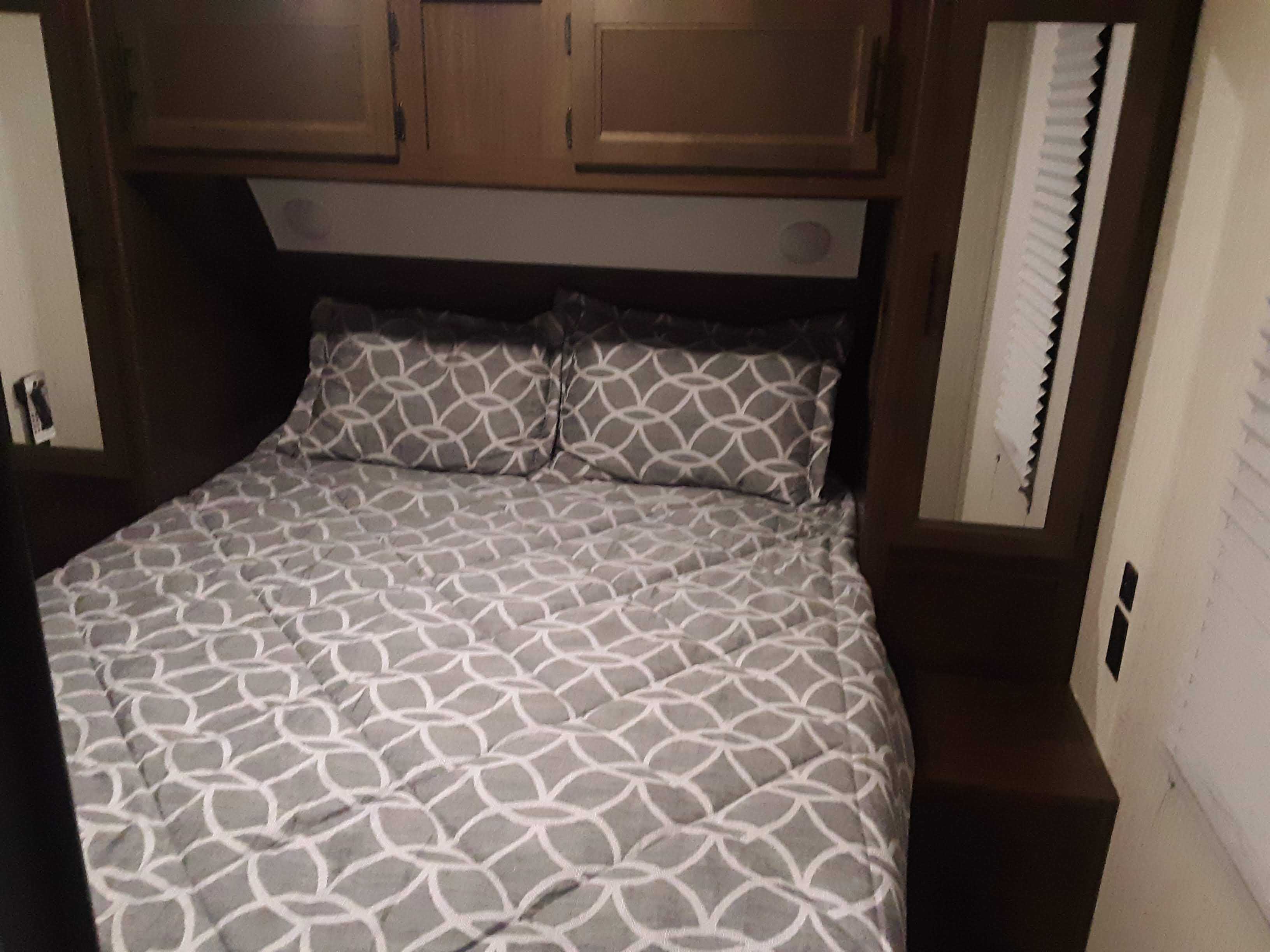 Cozy RV rental bedroom with a comfortable bed, patterned bedding, overhead cabinets, and a side mirror.. Forest River Cherokee Grey Wolf 2020