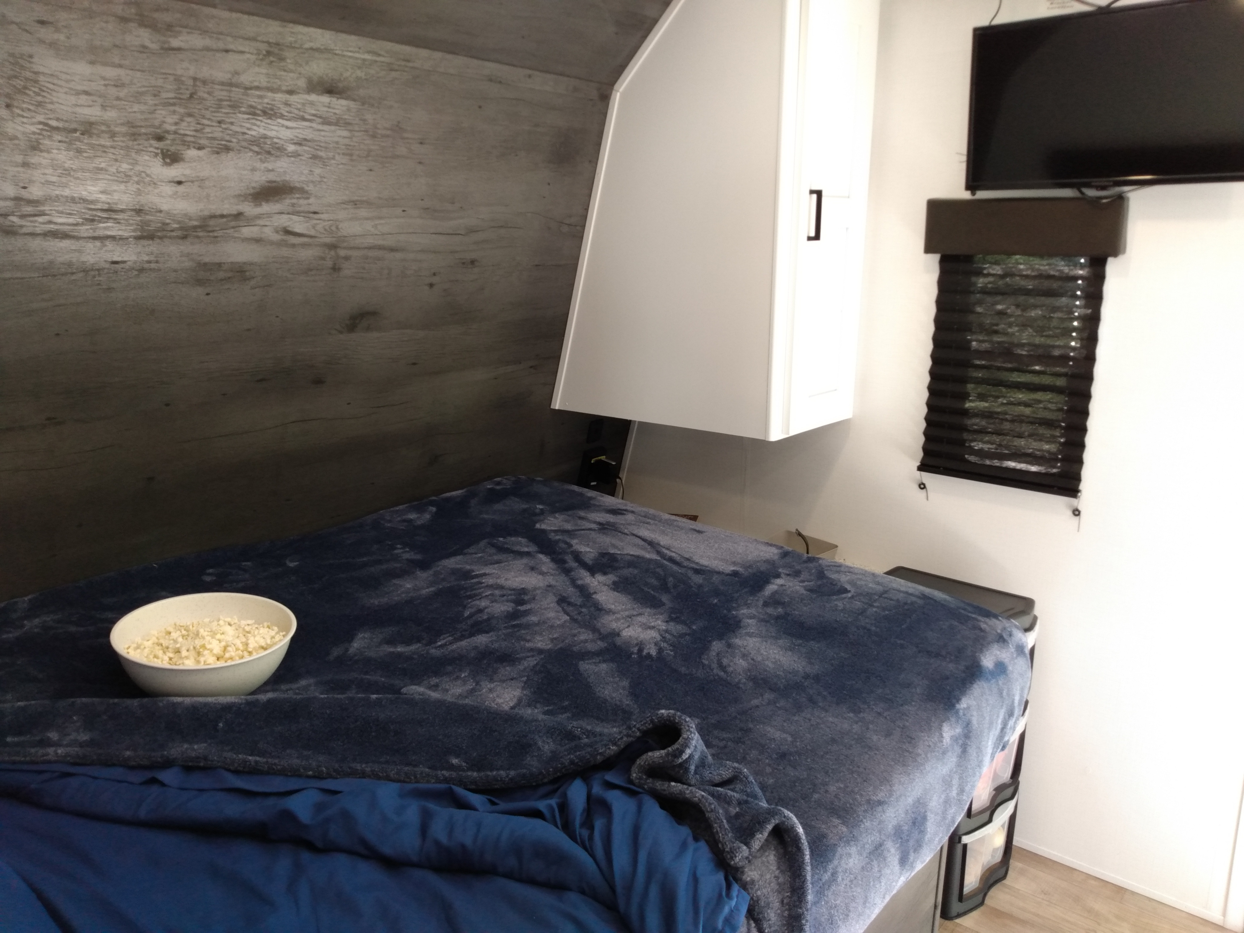 Cozy RV rental interior featuring a comfortable bed with popcorn, a mounted TV, and window blinds.. Keystone RV Hideout 2022