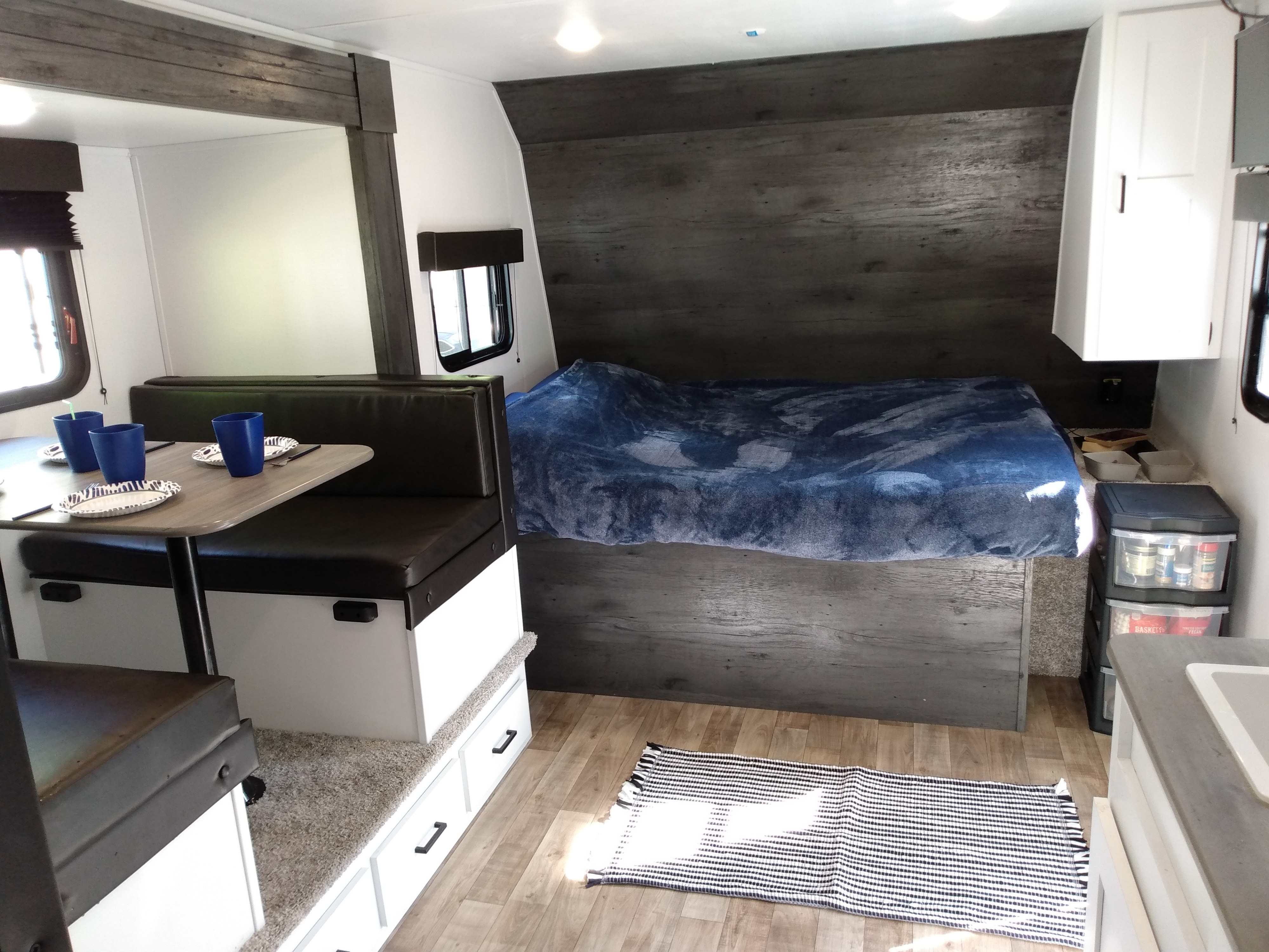 This modern rv rental features a cozy dinette, a comfortable bed with wood-paneled walls, and a compact kitchen setup.. Keystone RV Hideout 2022