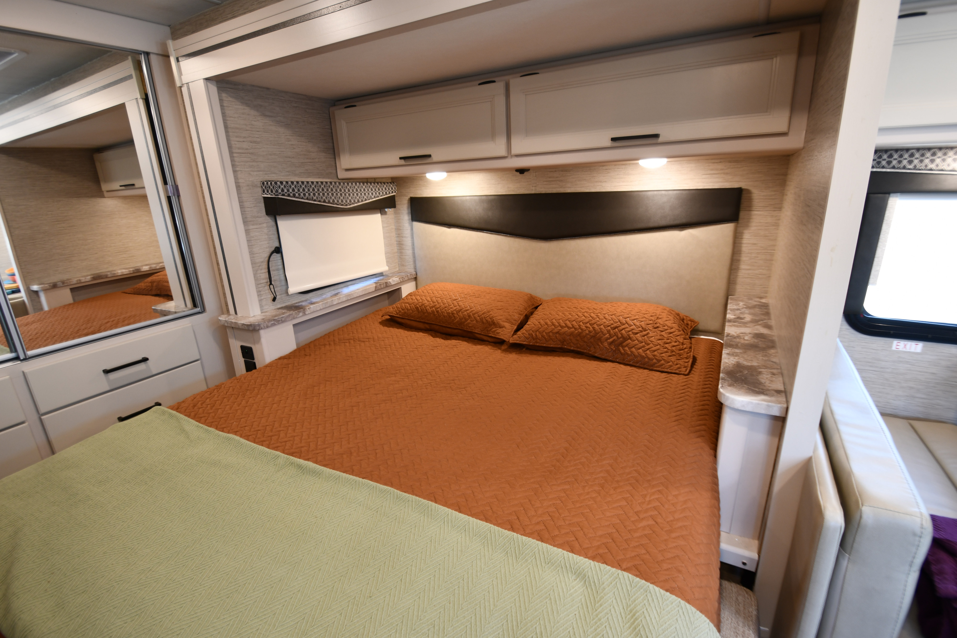Cozy RV rental bedroom featuring a bed with orange bedding, overhead cabinets, and mirrored closet.. Thor Compass 2022