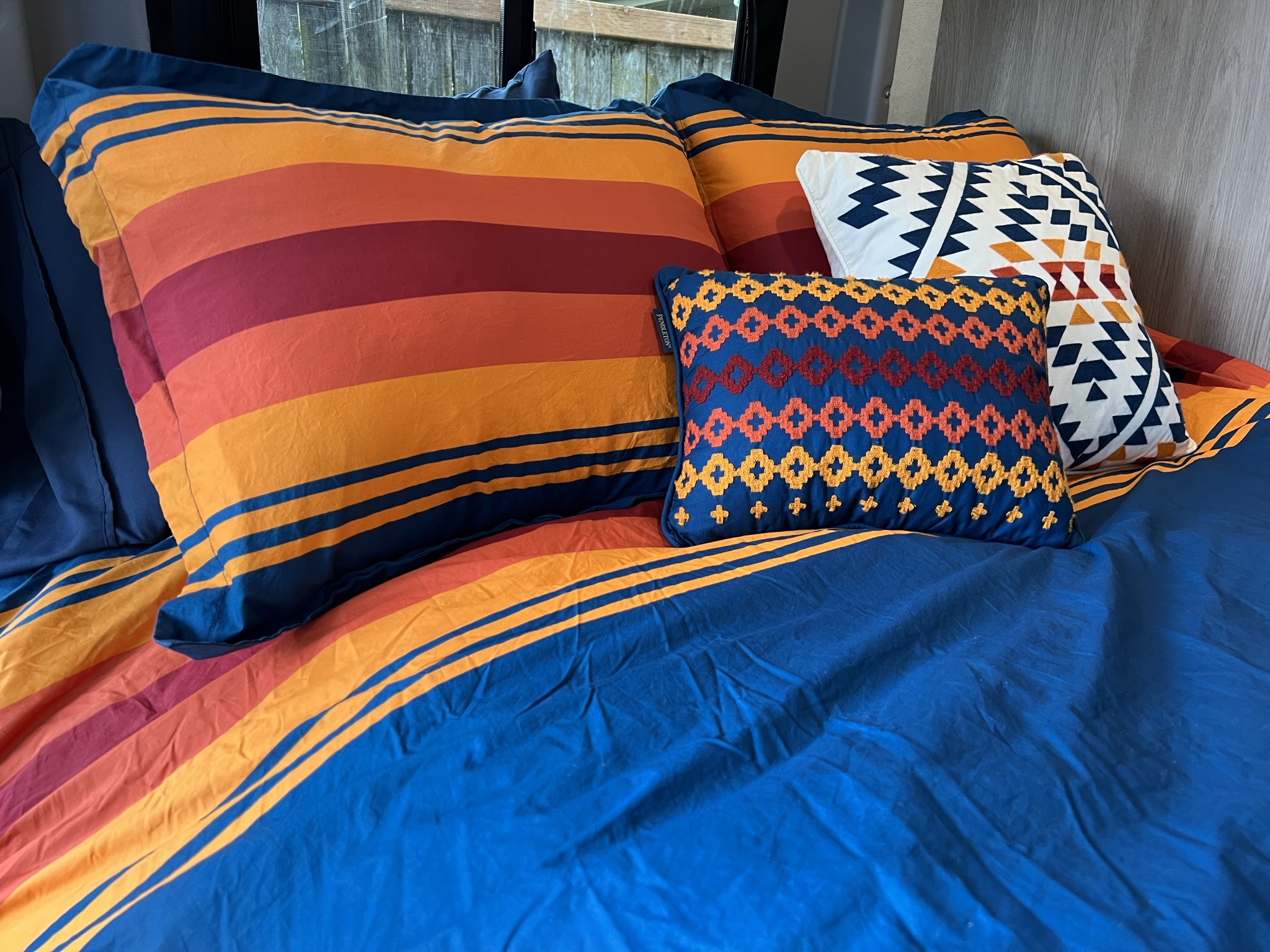 Cozy rv rental bedroom features vibrant striped bedding and Pendleton pillows, offering comfort in a compact interior space.. Winnebago Solis 2022