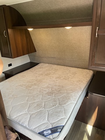 RV rental bedroom featuring a compact bed with a patterned mattress, built-in side tables, overhead cabinets, and lights.. Jayco Jay Flight 2018