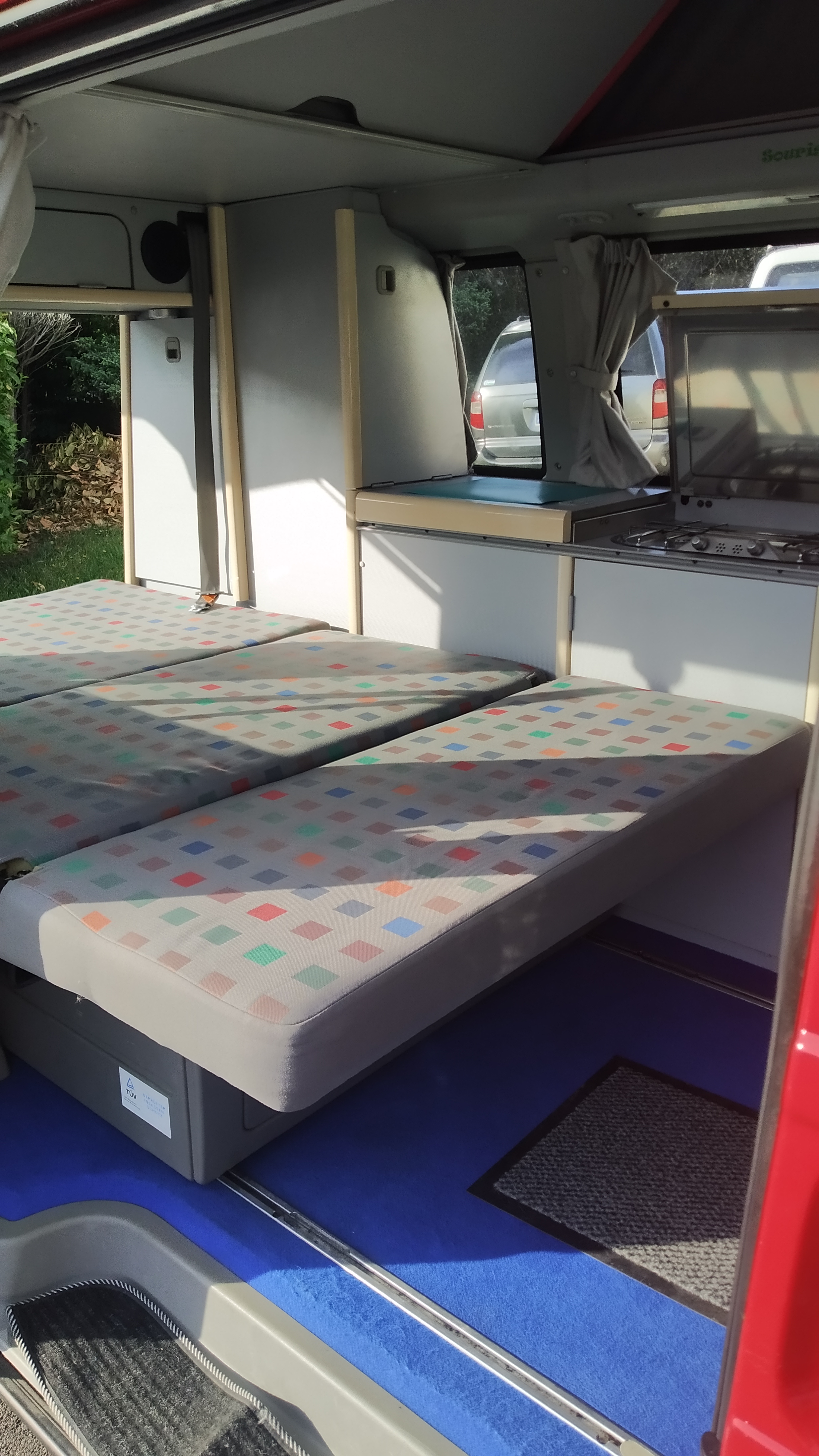 Inside an RV rental, showing versatile bed/seat cushions, a compact kitchen with stovetop, and overhead storage, ready for travel.. Volkswagen CALIFORNIA 2002