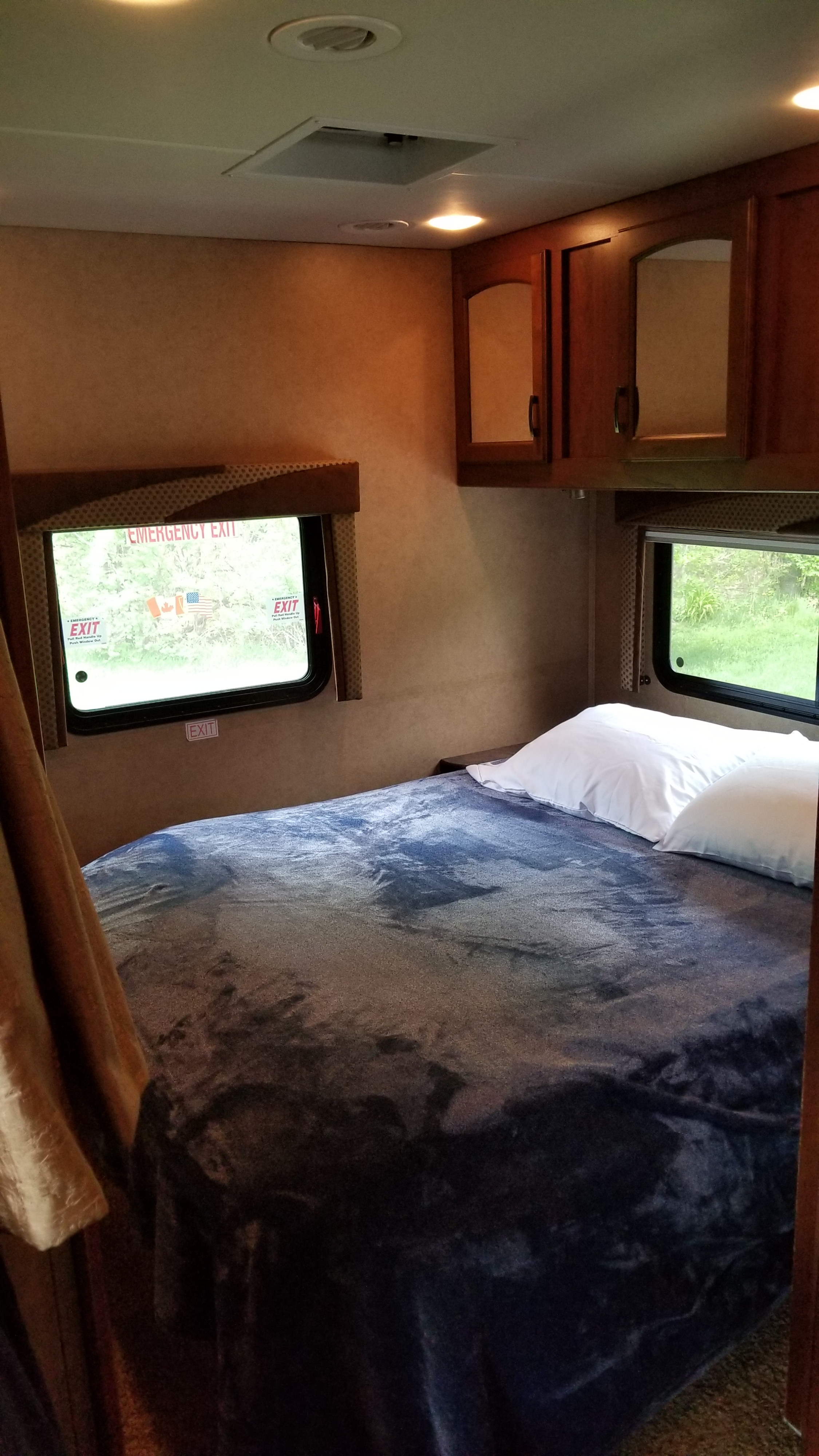 Cozy RV rental interior: a bedroom with a bed, two windows showing an emergency exit, and overhead wood cabinets.. Jayco Greyhawk 2013