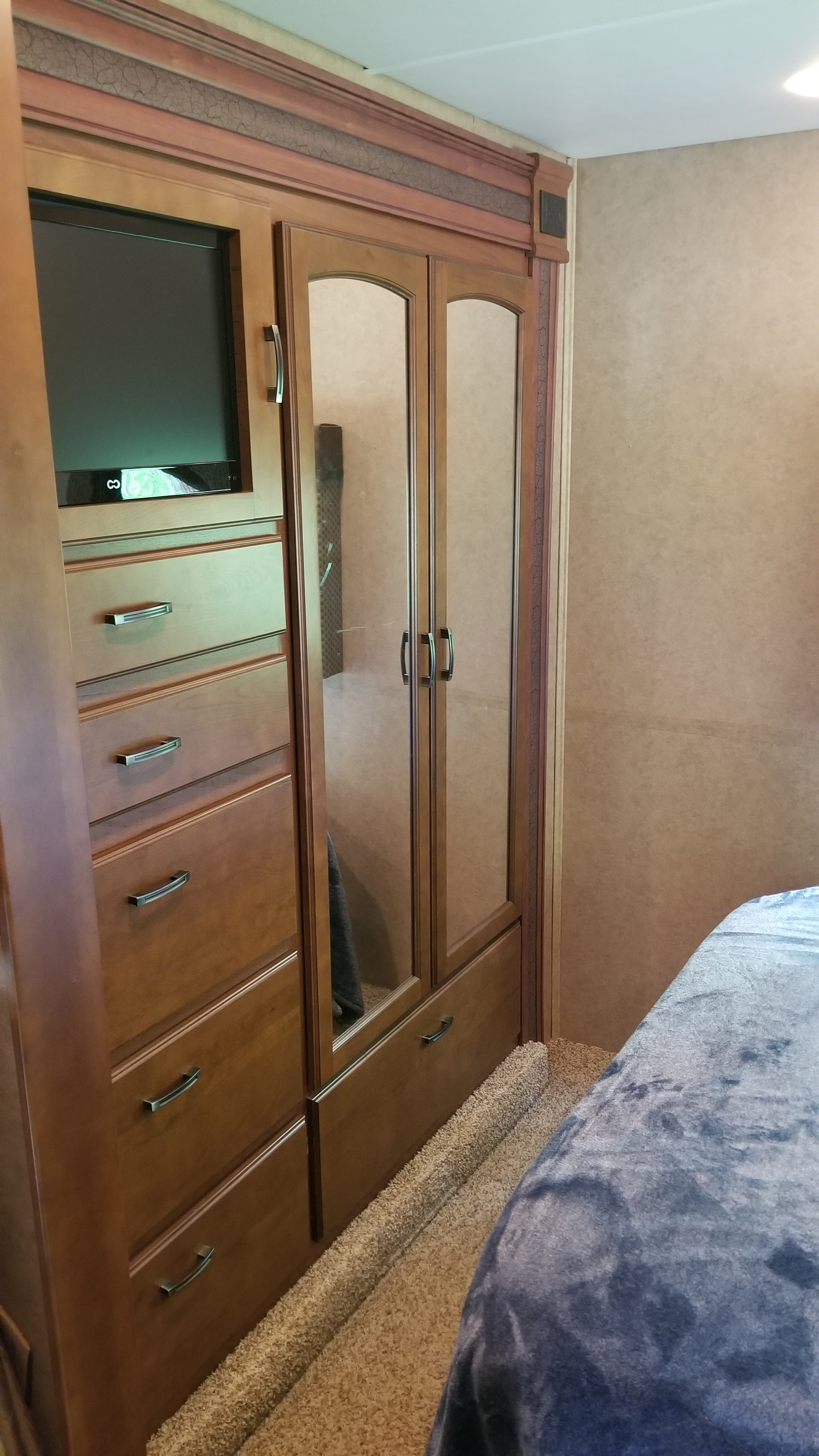 This RV rental interior showcases a bedroom with a built-in wooden cabinet, TV, mirrored wardrobe, dresser drawers, and a cozy bed.. Jayco Greyhawk 2013