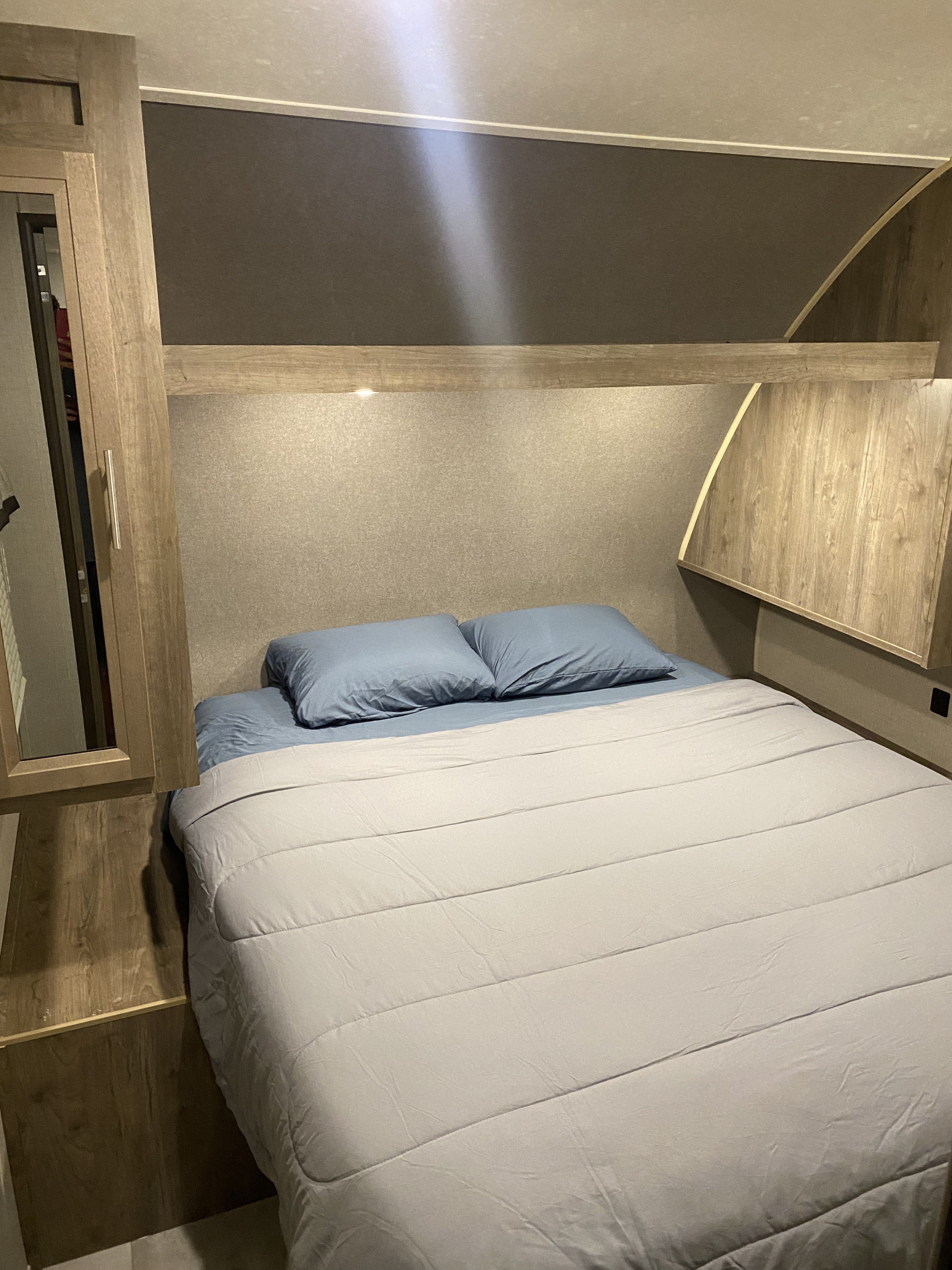 Comfortable RV rental bedroom featuring a bed with light blue bedding, wooden accents, and integrated lighting.. Jayco Jay Flight 2021
