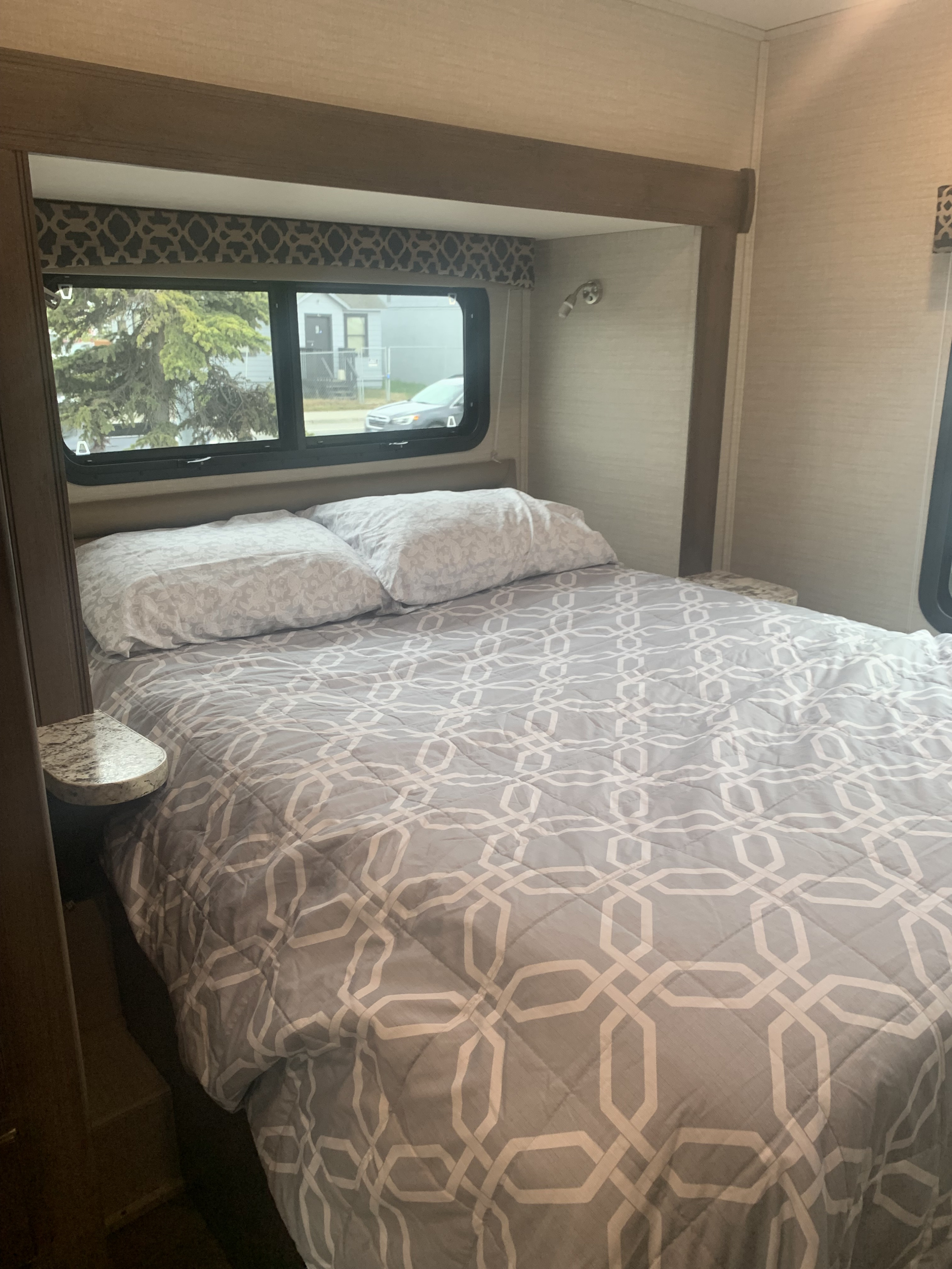 An RV rental's bedroom, featuring a bed with a gray geometric comforter, pillows, and a window view.. Jayco Redhawk 2020