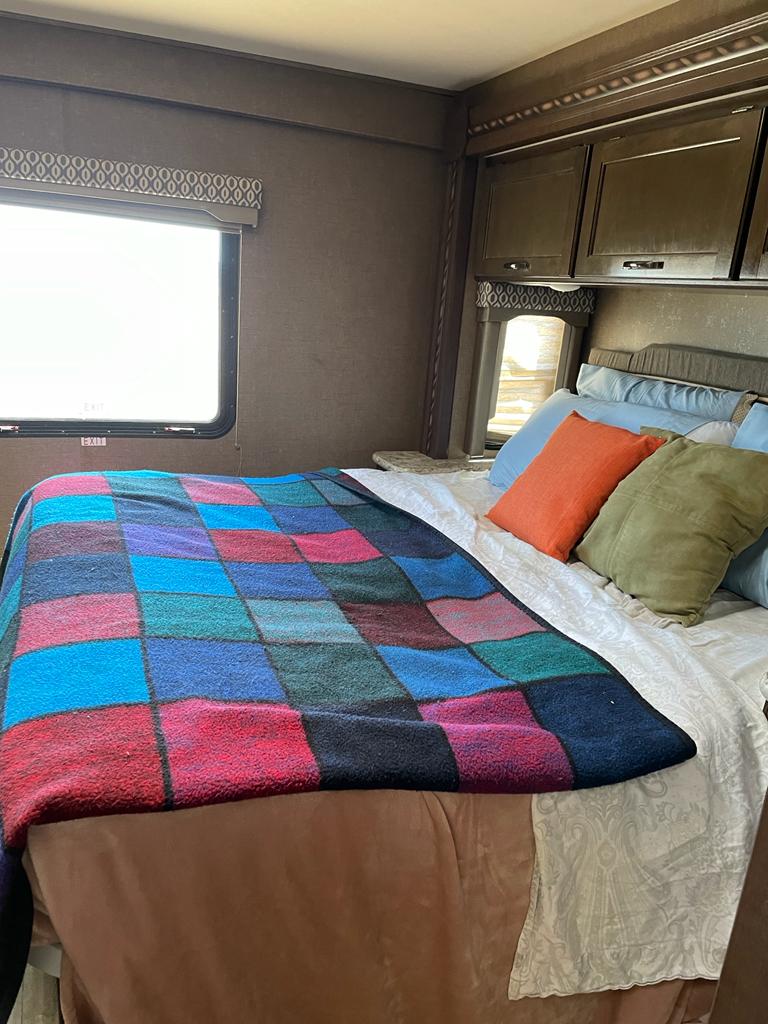 Cozy RV rental bedroom with a bed, colorful patchwork blanket, assorted pillows, and overhead storage cabinets.. Thor Motorcoach E450 Freedom Elite 2017