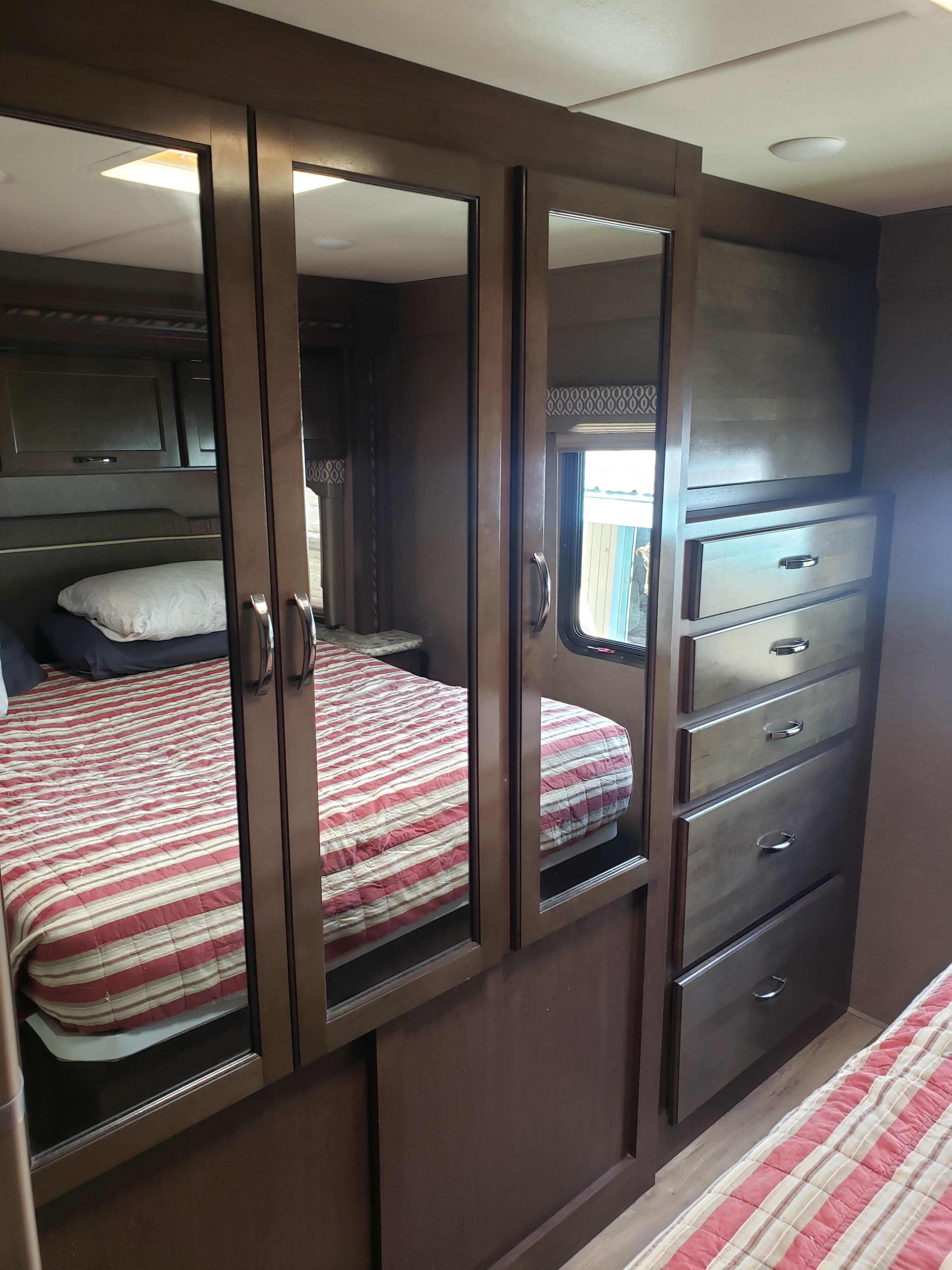 Inside an RV rental: compact bedroom with a striped bed, mirrored wardrobe, and storage drawers for comfortable travel.. Thor Motorcoach E450 Freedom Elite 2017
