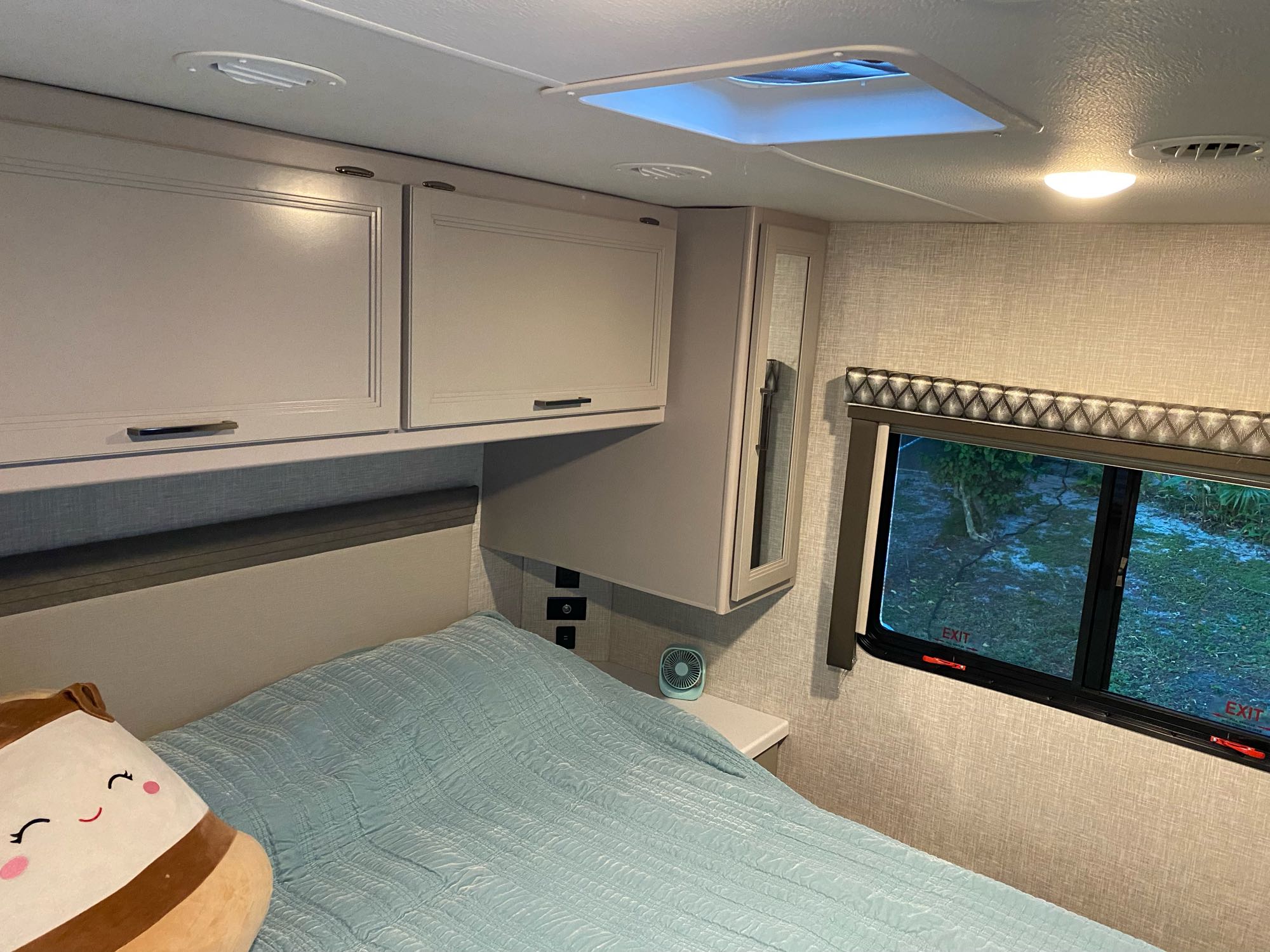Cozy RV rental bedroom featuring a comfy bed, overhead cabinets, and a window with an outdoor view for your next adventure.. Thor Quantum LC28 2022