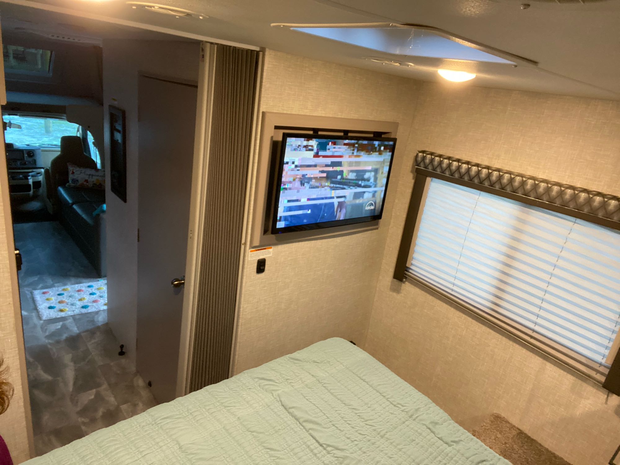 Cozy RV rental bedroom with light blue bed, mounted TV, and window. Ideal for road trips and comfortable stays.. Thor Quantum LC28 2022