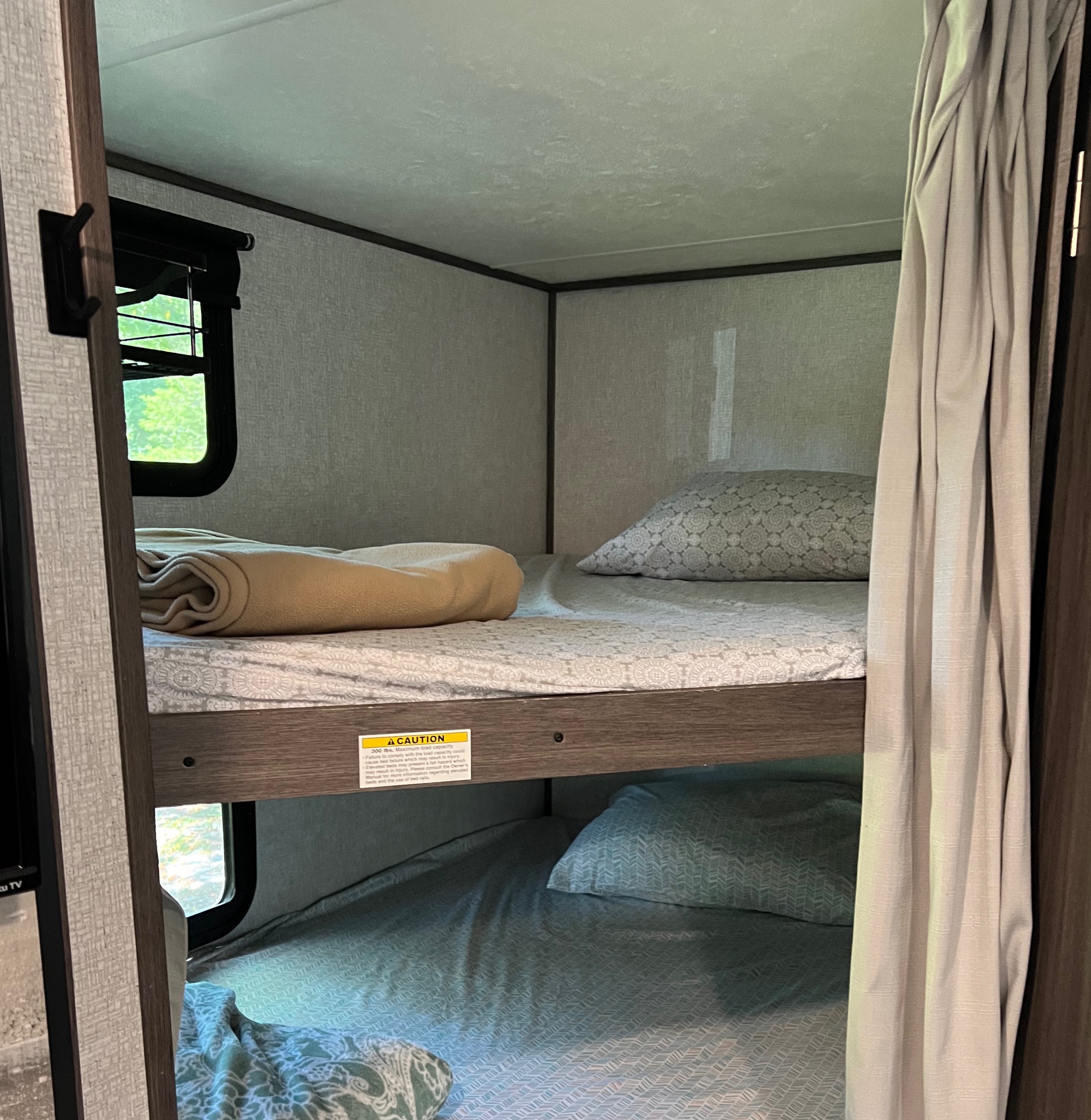 Inside an RV rental, two cozy bunk beds with patterned bedding and pillows await. Perfect for family travel adventures!. Dutchmen Kodiak SE 2021
