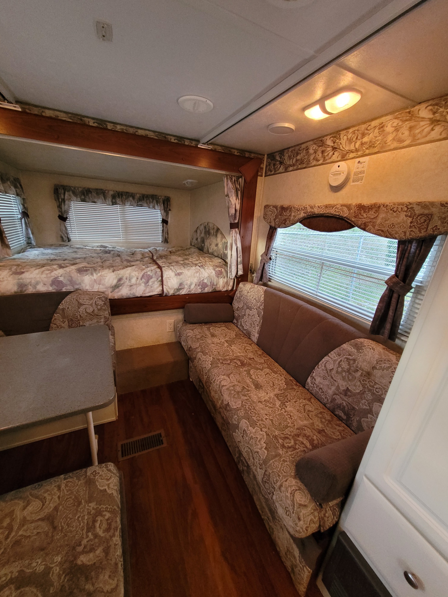 An inviting RV rental interior with a raised bed, dinette, and sofa, offering a complete and compact living space.. Keystone RV Outback 2009
