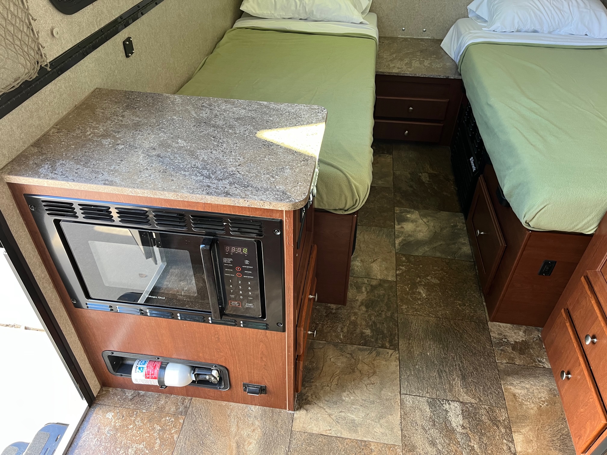 Inside an RV rental, twin beds, a built-in microwave, and a fire extinguisher for road trip safety.. Forest River Flagstaff 2017