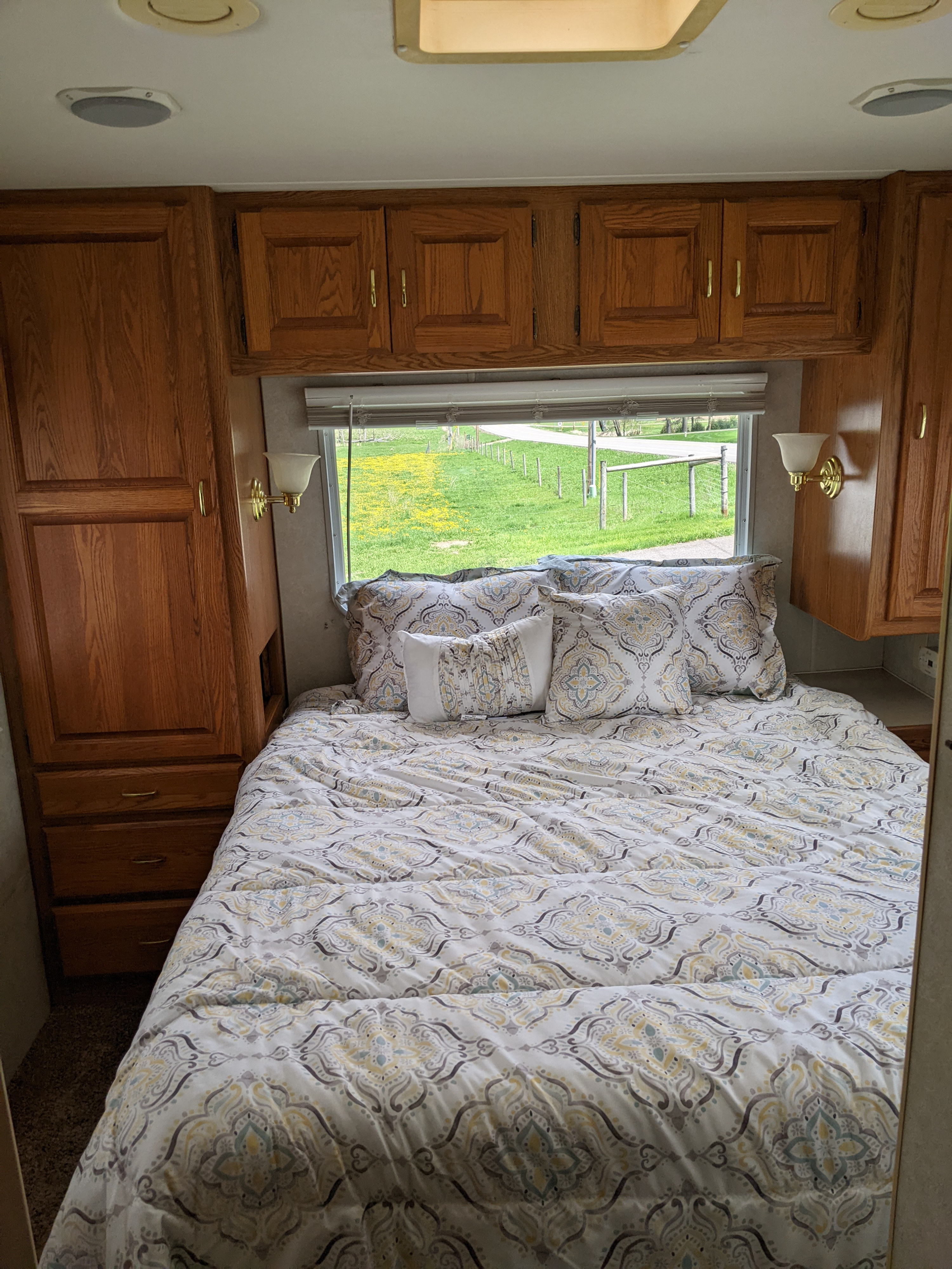 Cozy RV rental bedroom featuring patterned bedding, wooden built-in storage, and a scenic window view of a grassy field.. Holiday Rambler Atlantis 2003
