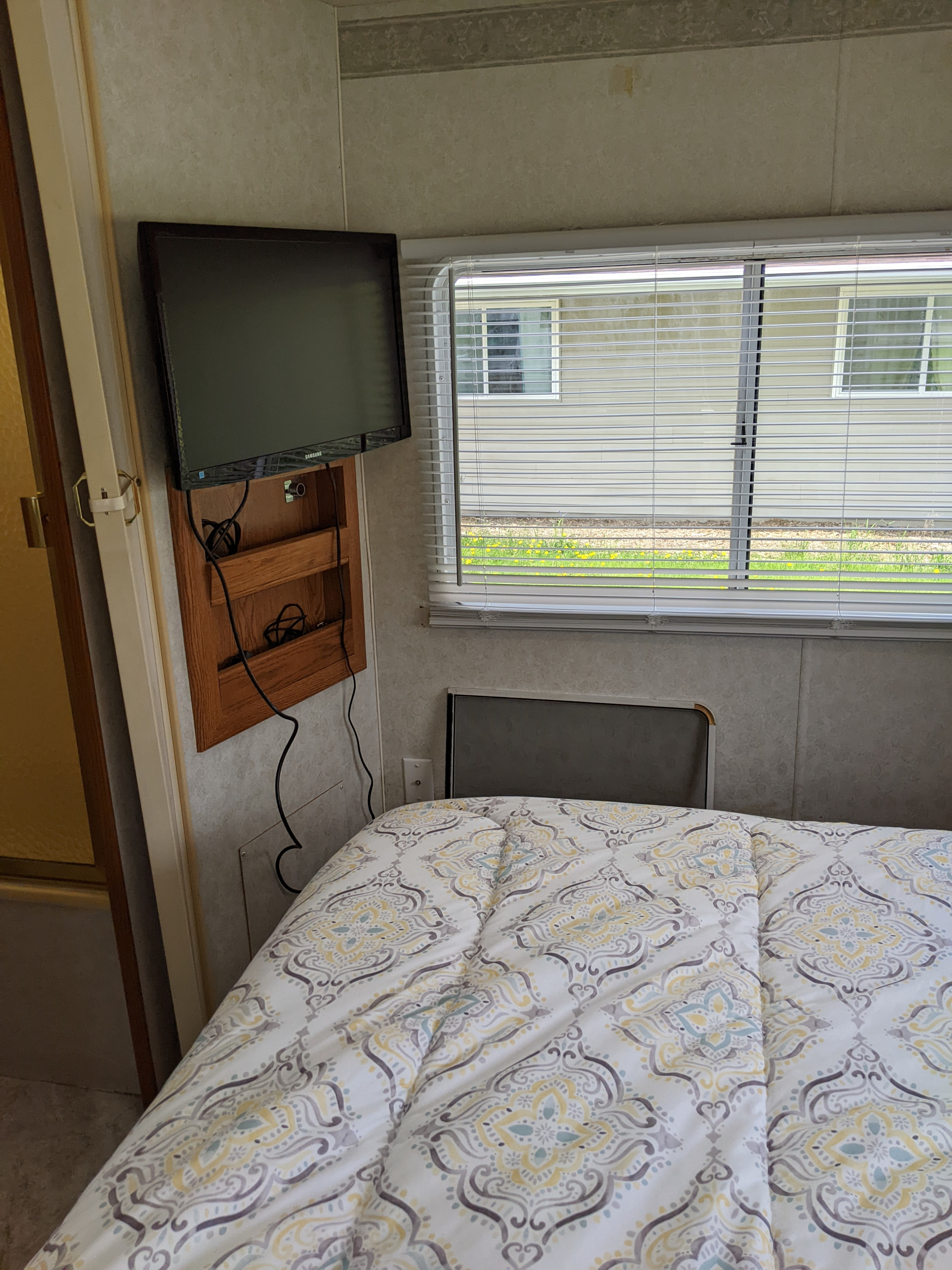 Cozy RV rental bedroom featuring a mounted TV, comfortable bed with patterned comforter, and window with blinds.. Holiday Rambler Atlantis 2003