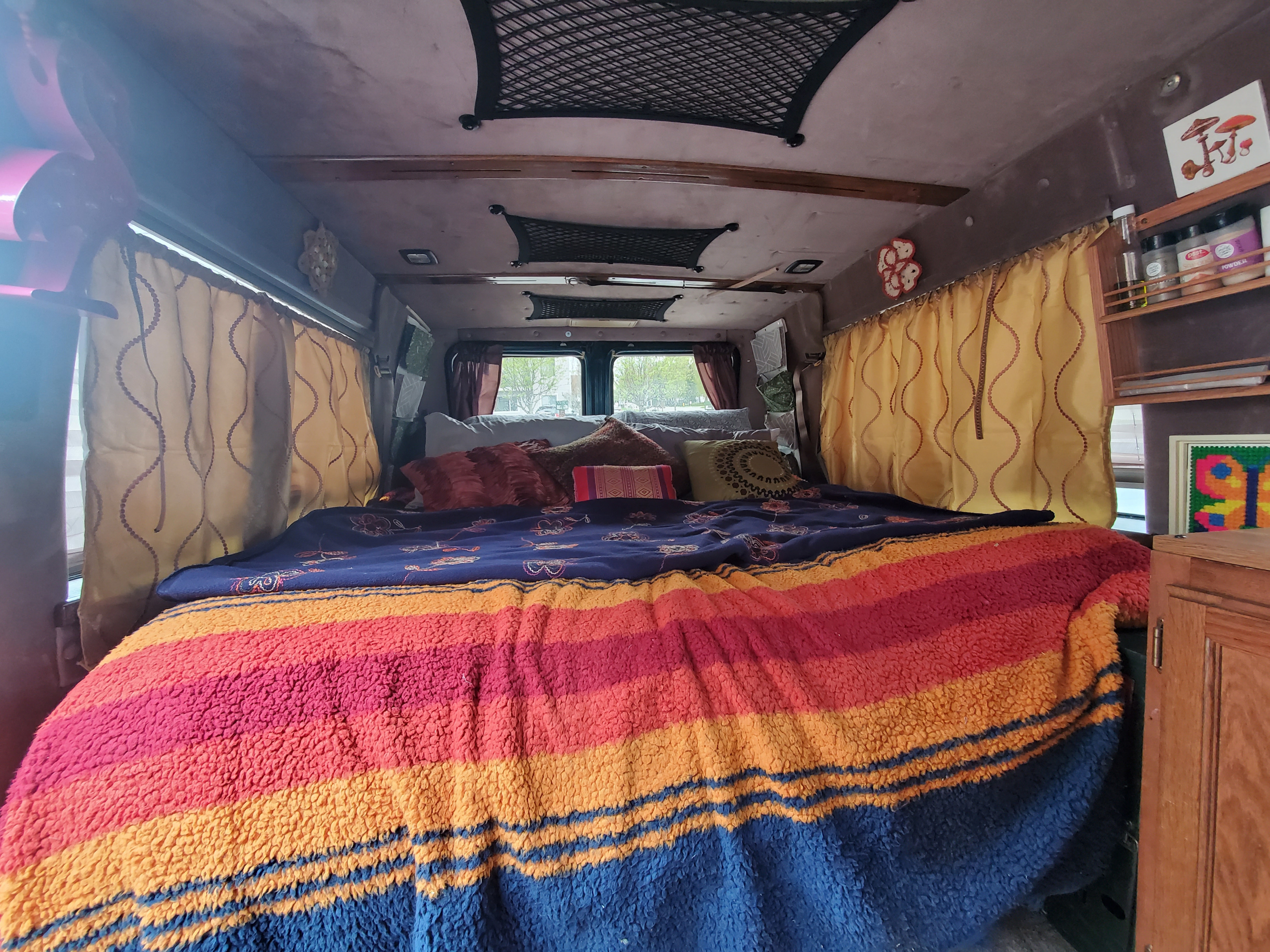 This inviting RV rental features a cozy bed with a cheerful striped blanket and eclectic decor.. Chevrolet G-20 1995