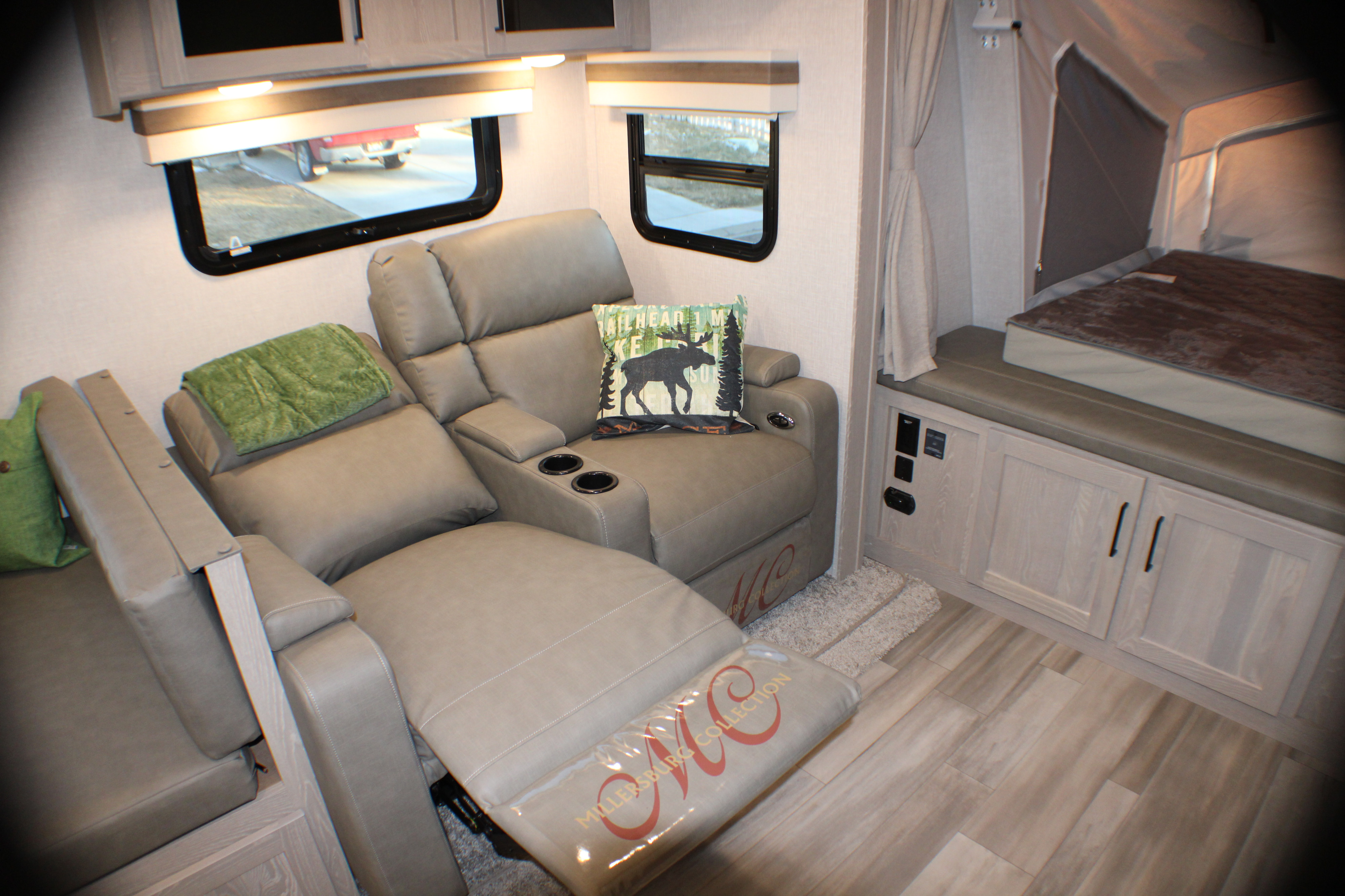 RV rental interior: comfortable recliners with cupholders, a moose pillow, wood-look flooring, and a cozy bed area. Millersburg Collection.. Forest River Rockwood Roo 2022