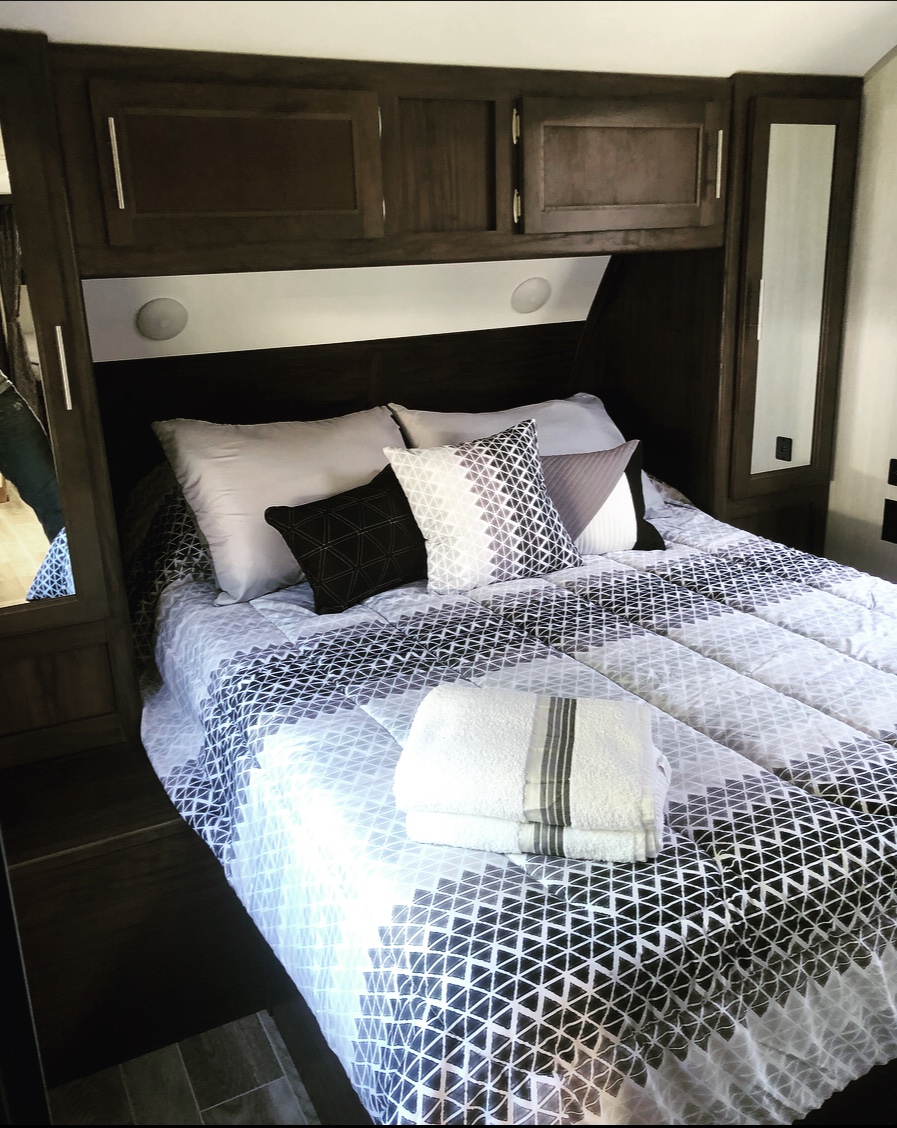 Cozy RV rental bedroom featuring modern geometric bedding, stacked towels, and built-in storage cabinets.. Forest River Cherokee Grey Wolf 2019