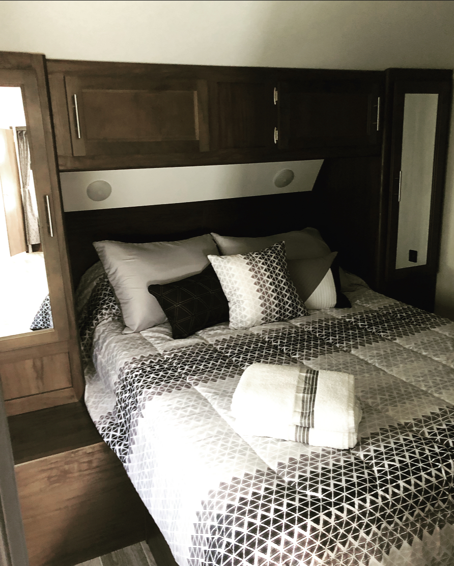 Cozy RV rental bedroom with geometric bedding, overhead cabinets, and integrated lighting.. Forest River Cherokee Grey Wolf 2019