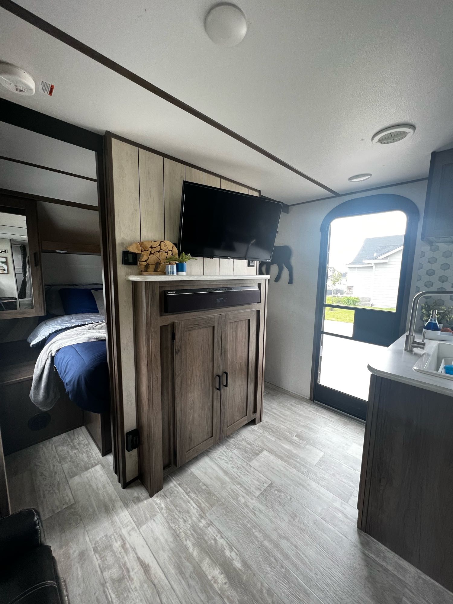 Modern RV rental interior showing bedroom, TV, and kitchen. Light wood-look flooring, compact living space.. Forest River Tracer LE 2020