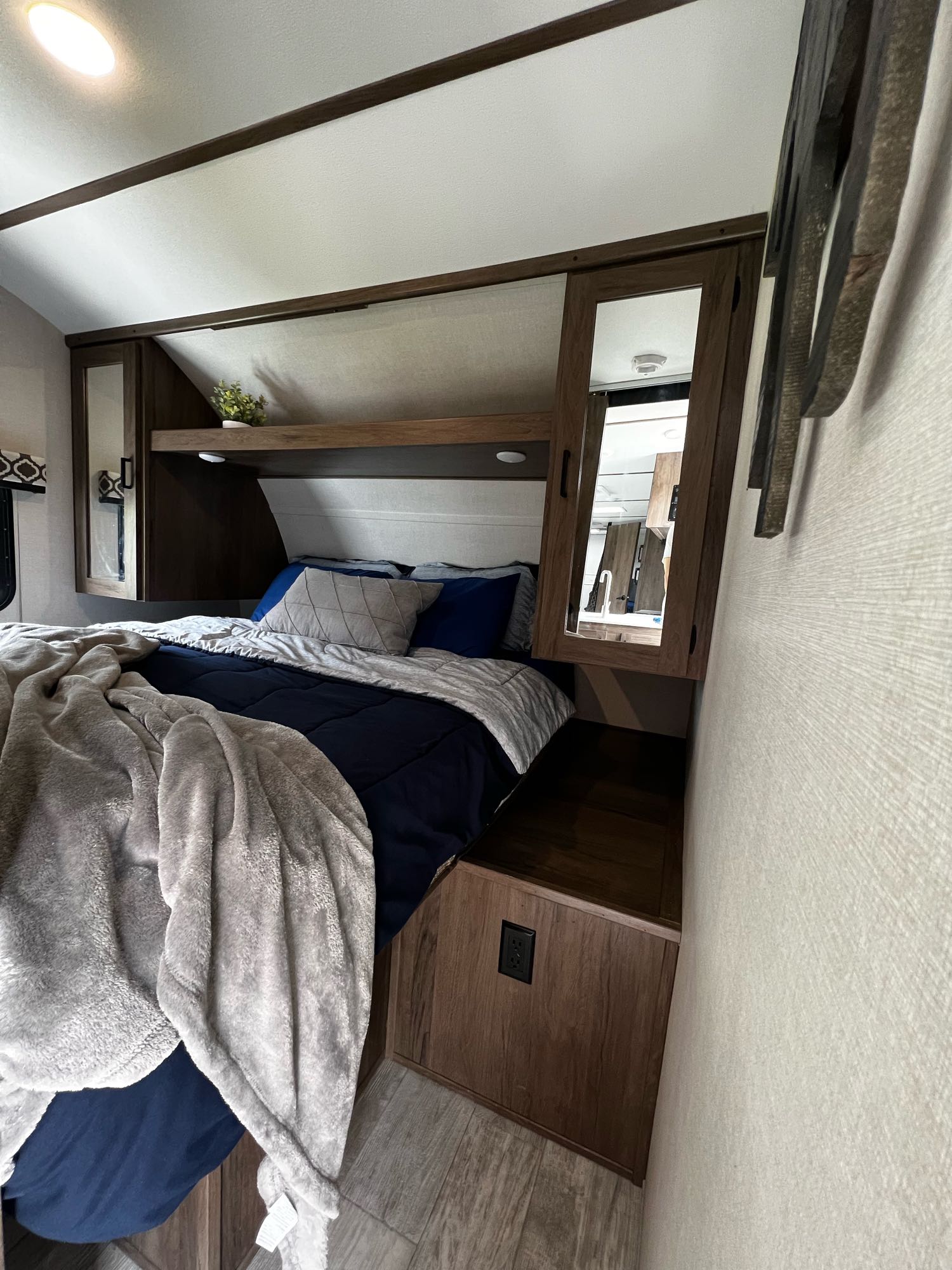 Cozy RV rental bedroom features a comfy bed with navy/grey bedding, overhead storage, and warm wood accents.. Forest River Tracer LE 2020
