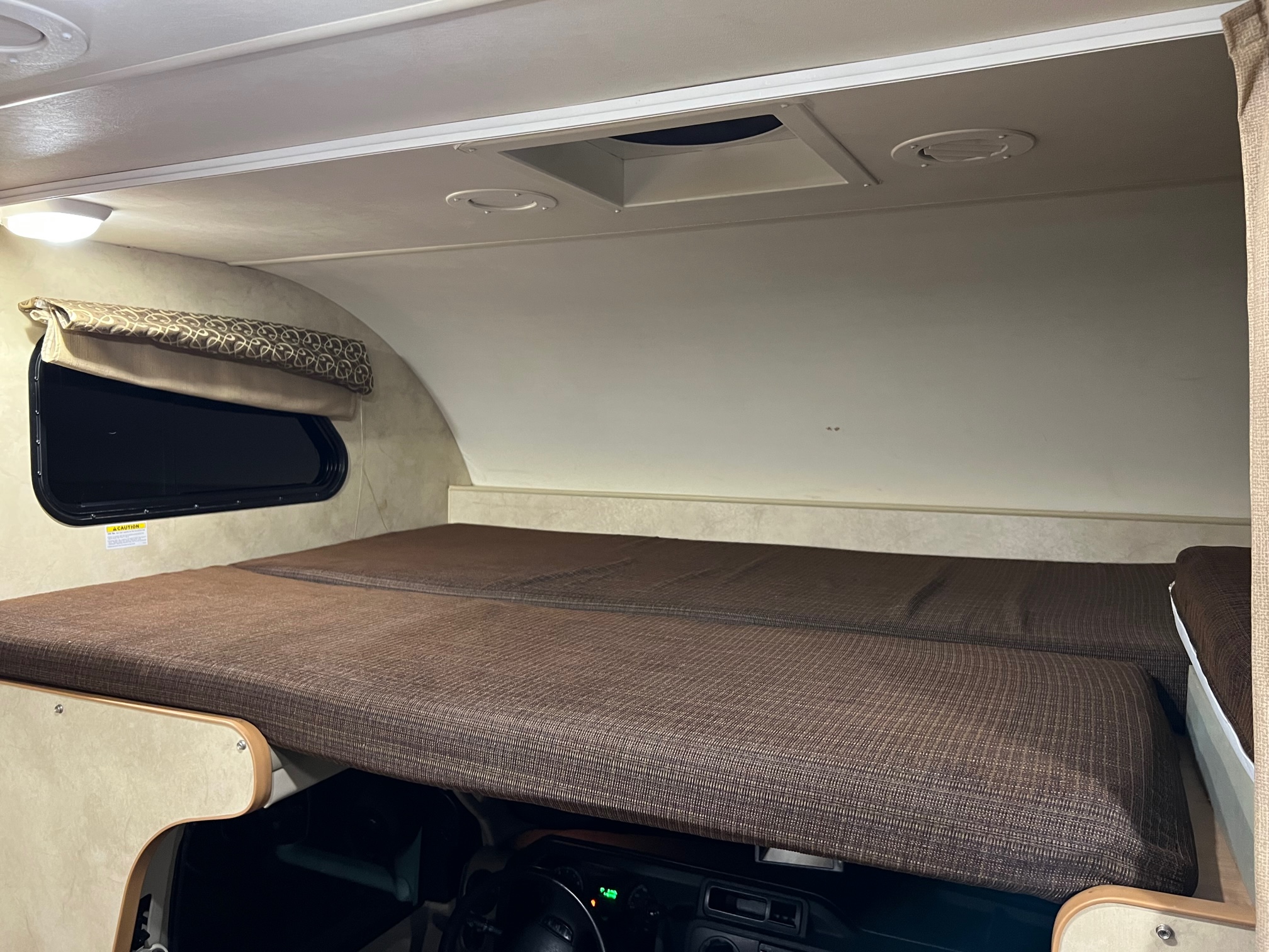 Inside an RV rental: a spacious cab-over bunk bed with brown cushions, a side window, and ceiling vents.. Thor Four Winds 2013