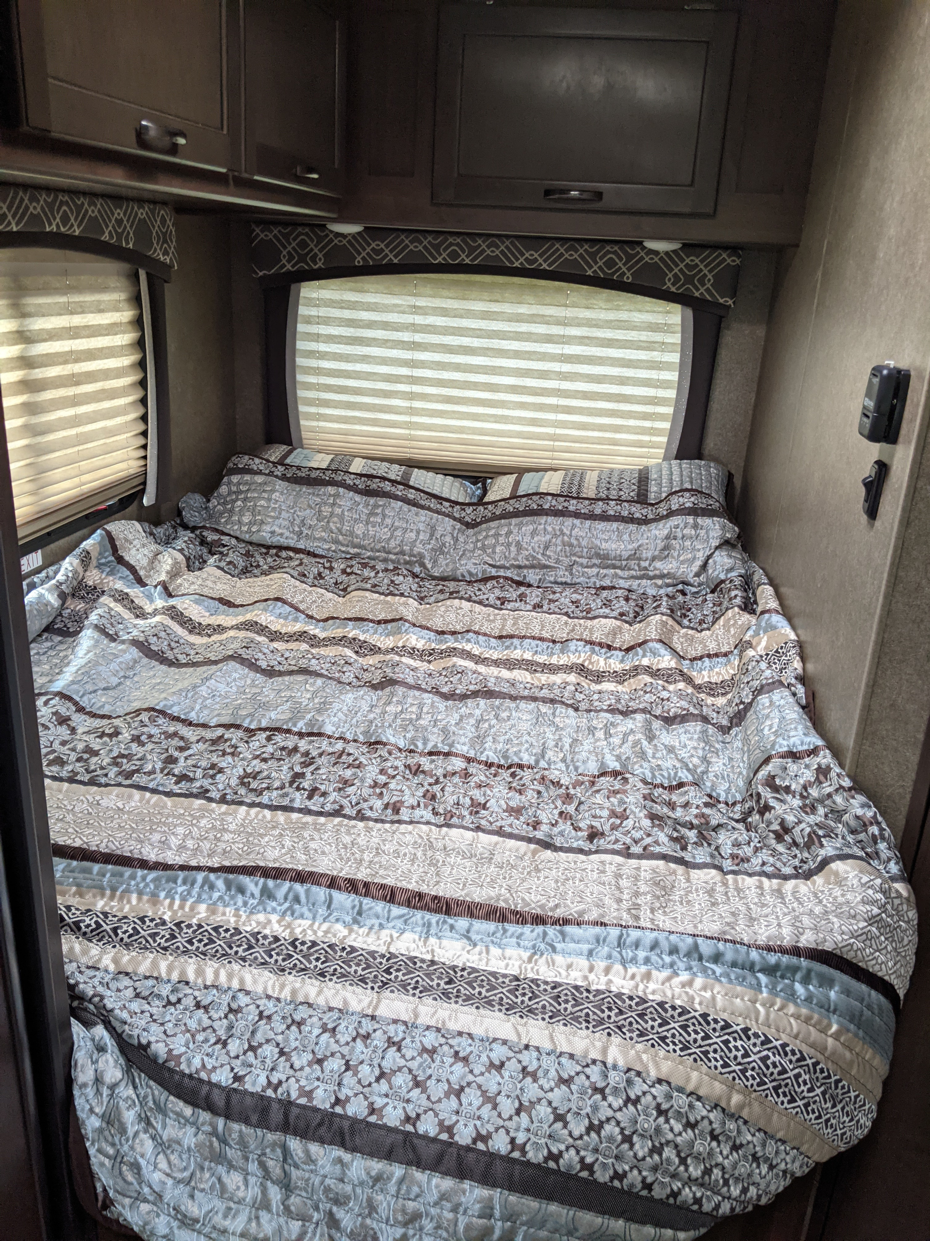 Inviting RV rental bedroom with a large bed, patterned comforter in blues, browns, and whites, windows, and cabinets.. Thor Chateau 2020