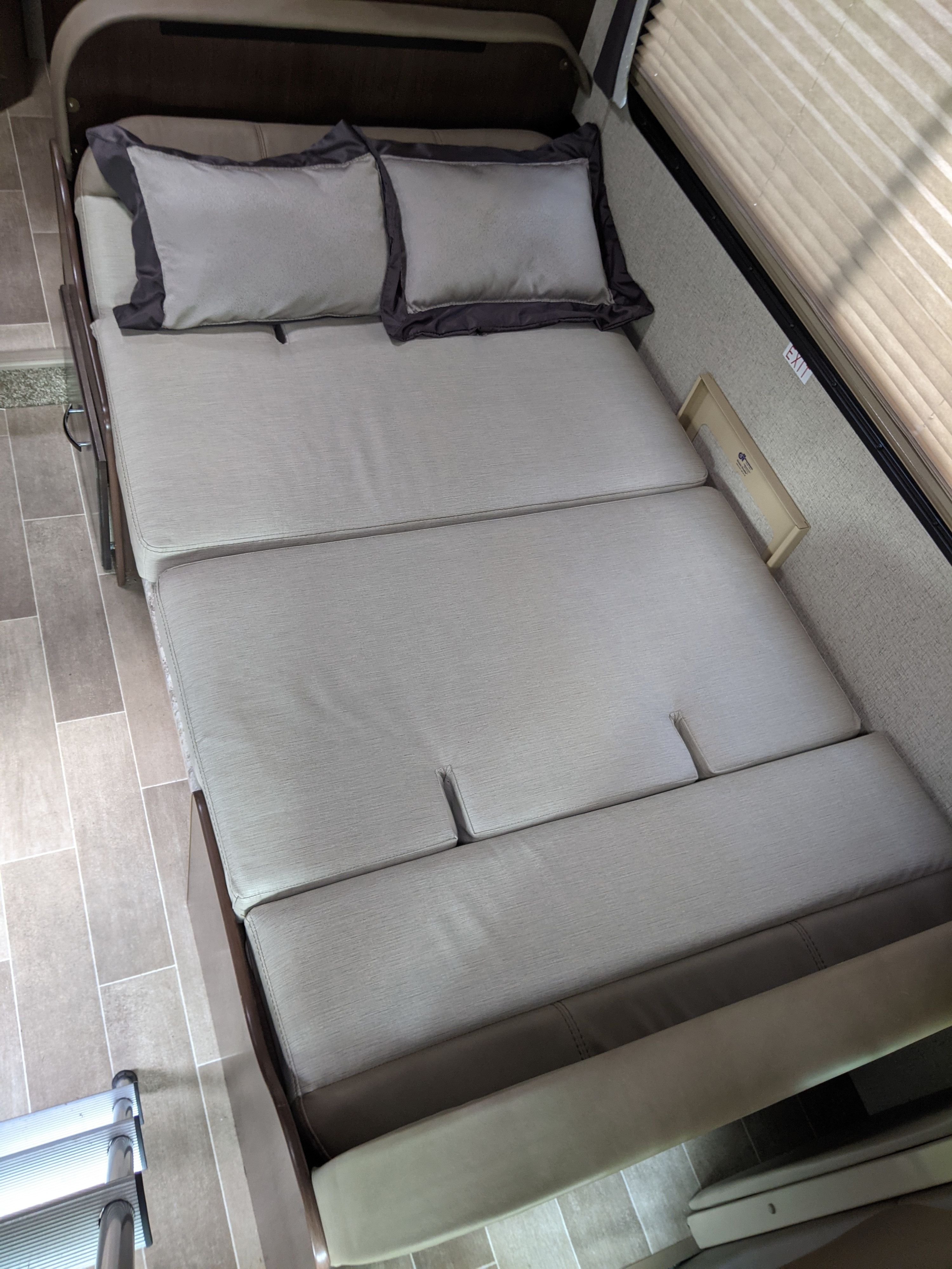 An RV rental pull-out bed, made of light-colored fabric cushions with pillows, extends into the room, showing tiled flooring.. Thor Chateau 2020