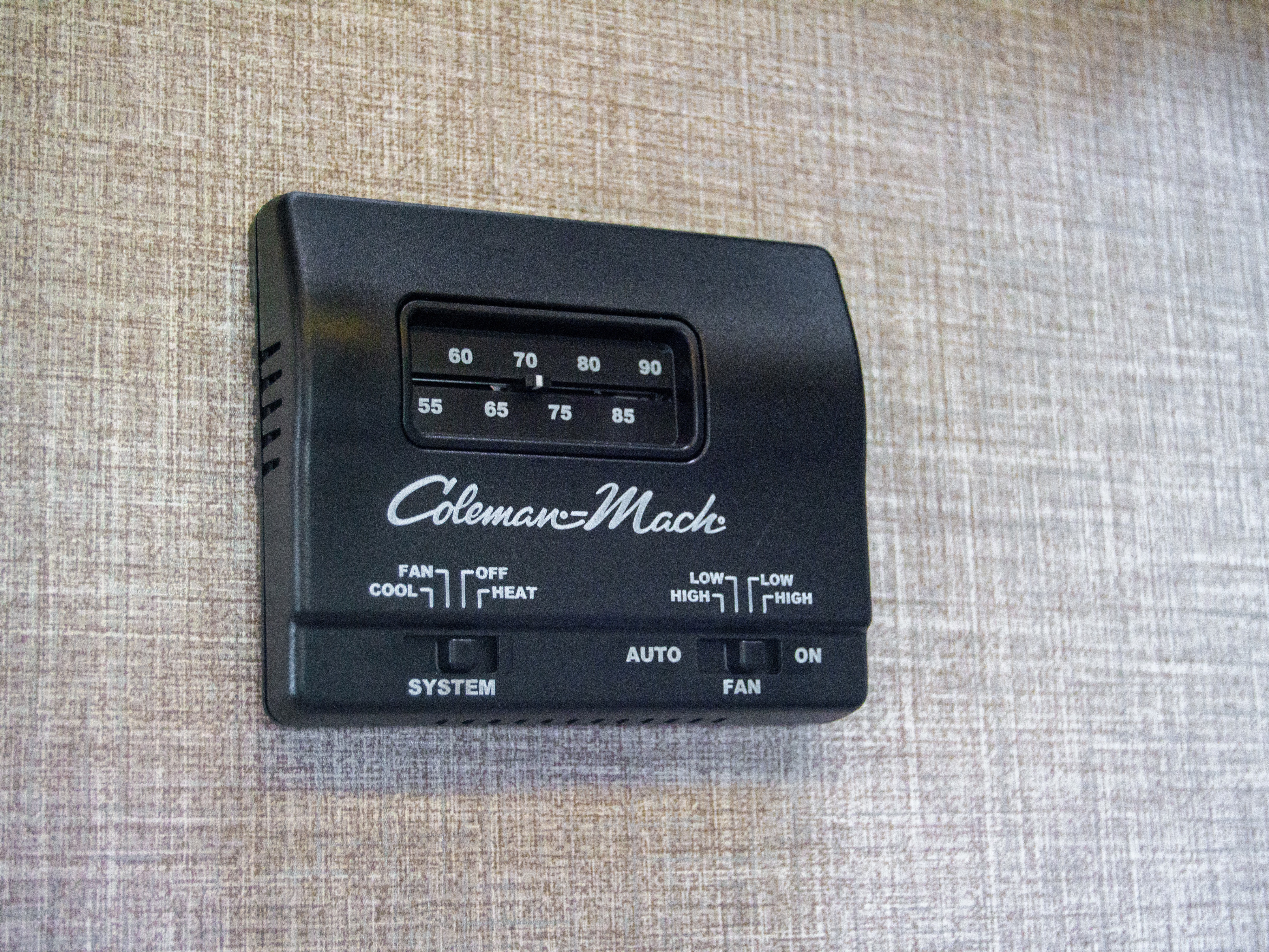 Black Coleman-Mach thermostat in an RV rental. Features a temp dial (55-90F) and sliders for system (Cool/Heat/Off) and fan controls.. Other Other 2022