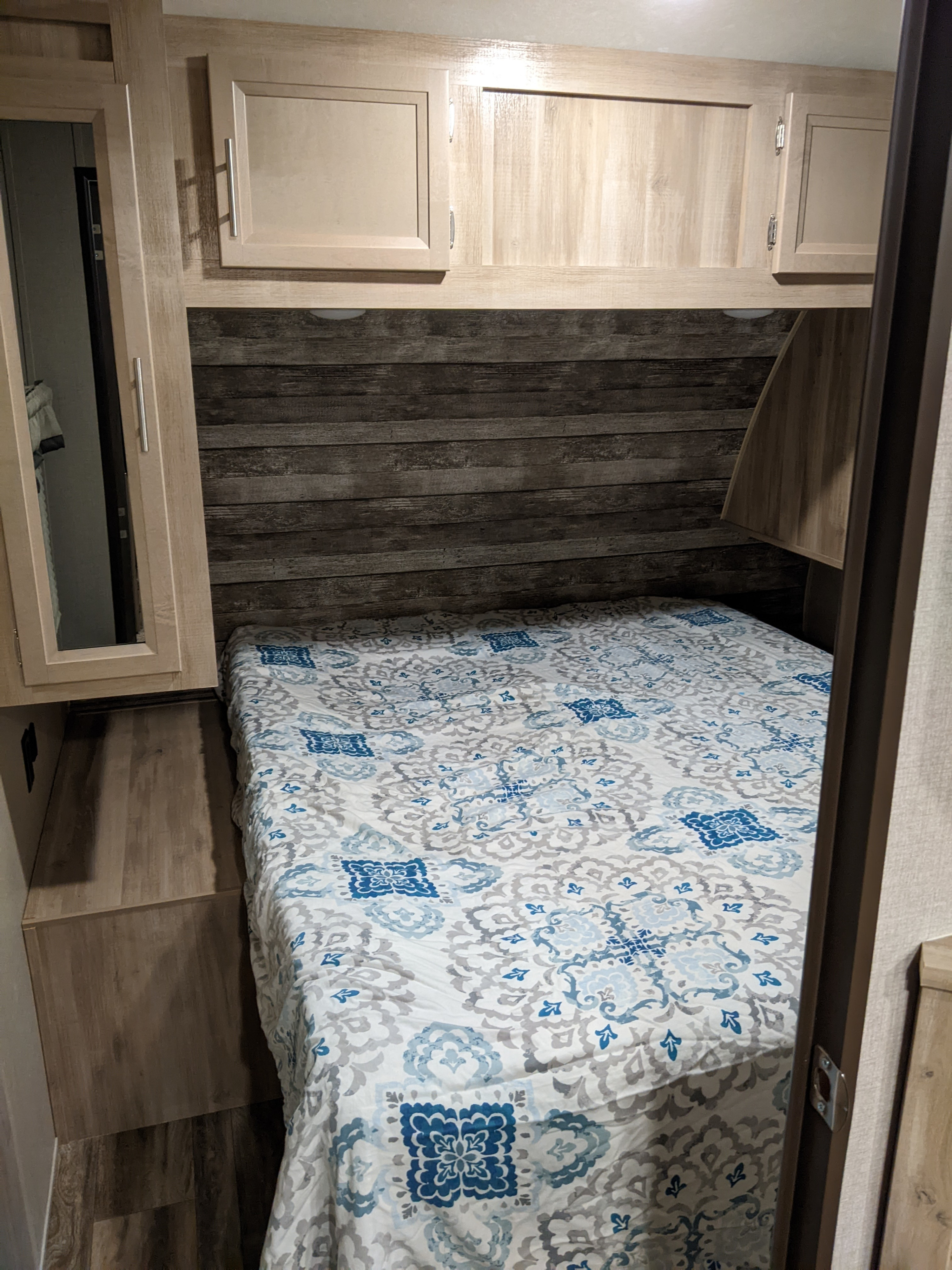 Inside an RV rental: a compact bedroom features a bed with blue & white bedding, rustic wood headboard, and storage cabinets.. Coachmen Catalina Legacy Edition 2020