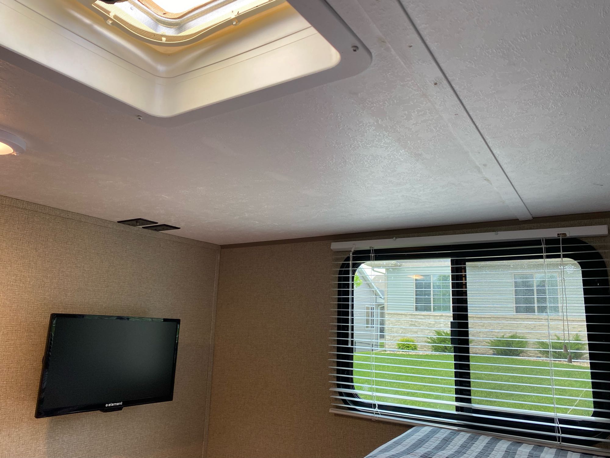 Experience an **rv rental**! Interior with a ceiling skylight, wall-mounted TV, and window with blinds showing a house and green yard.. Keystone RV Summerland 2018