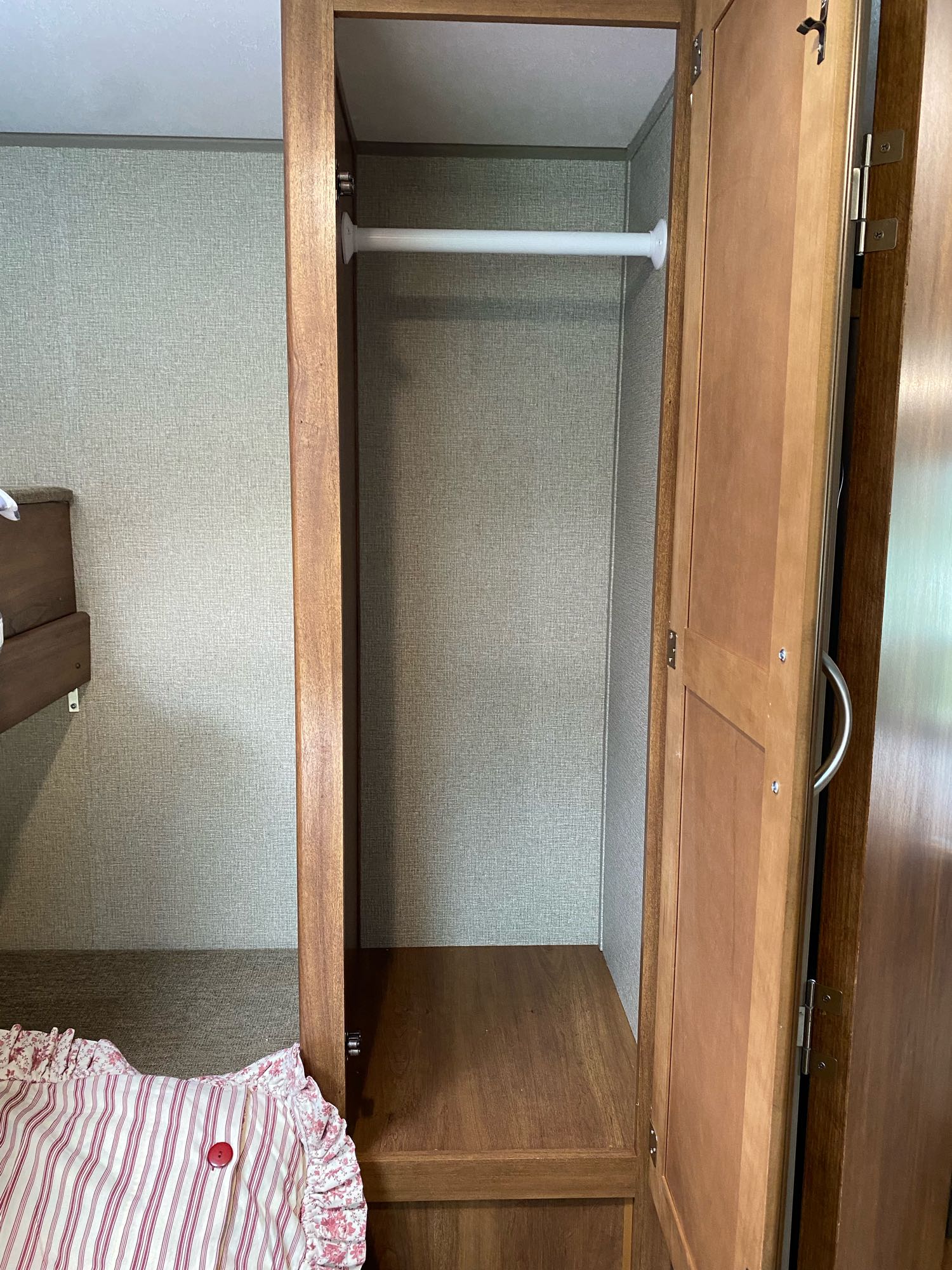 RV rental wardrobe: an open closet with a white hanging rod, providing clothes storage next to a bed with a striped pillow.. Keystone RV Summerland 2018