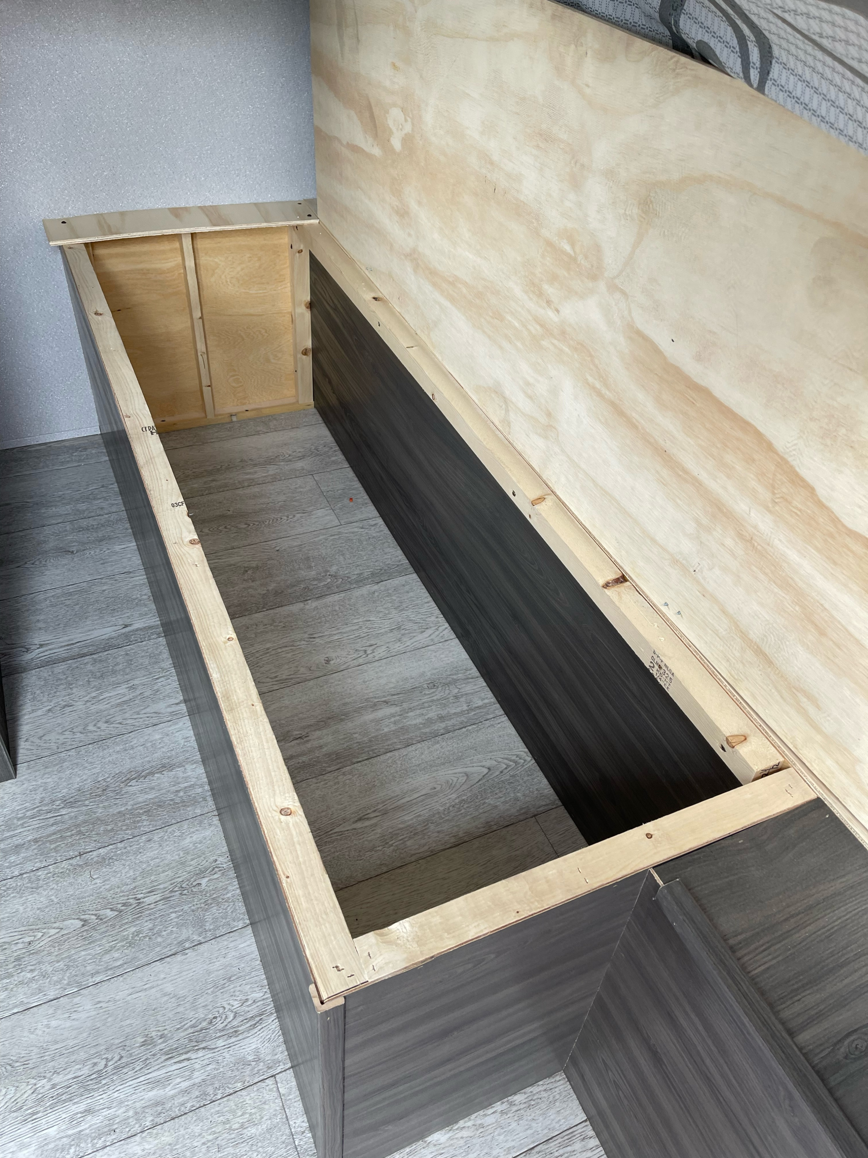 RV rental: custom storage bench under construction. Features exposed plywood framing and dark wood-look paneling.. Forest River Shasta 2021