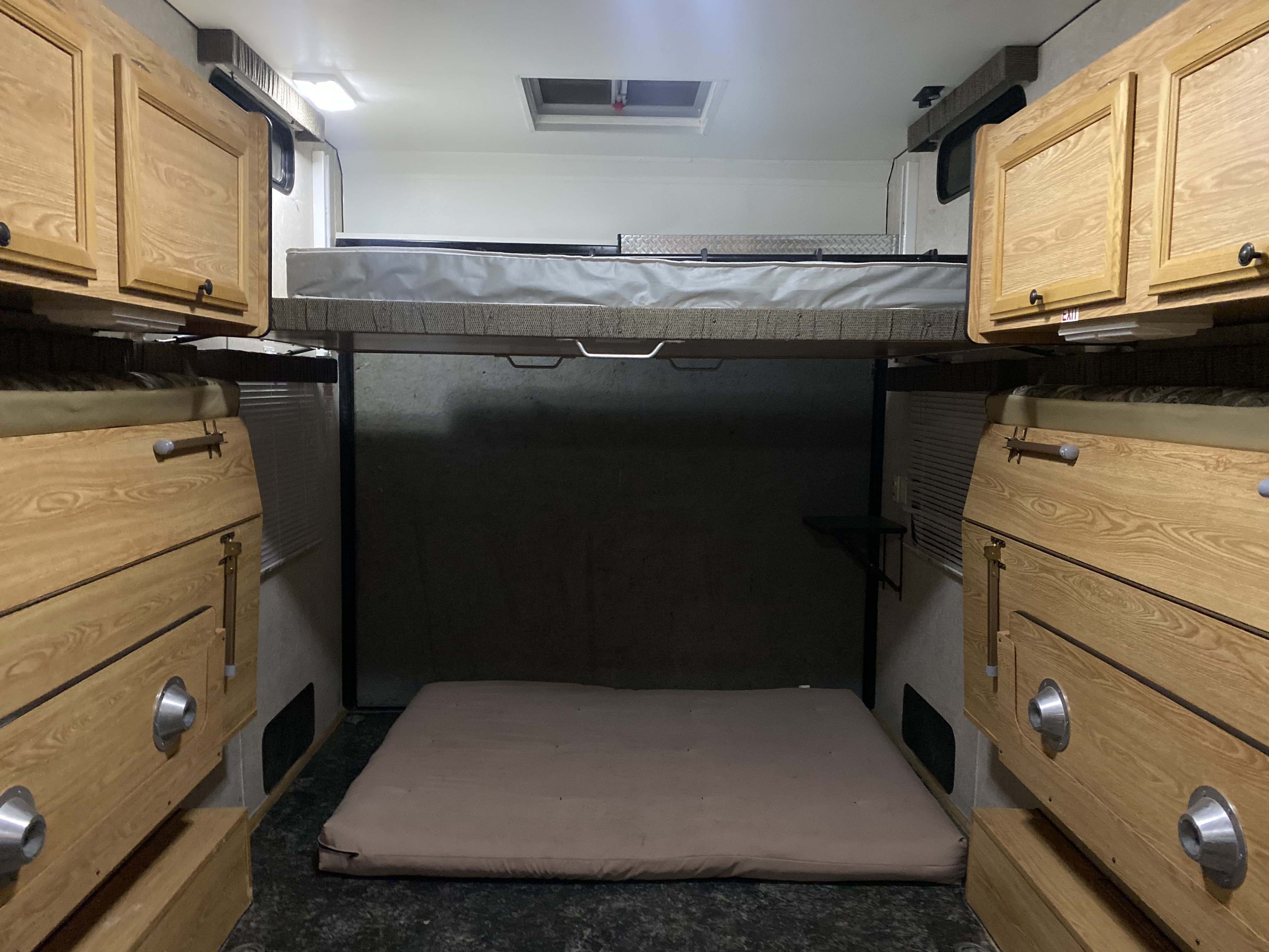 Bright RV rental interior with a raised bunk bed, a floor mattress, and wood cabinets on both sides.. Carson Trailer Fun Runner 2007