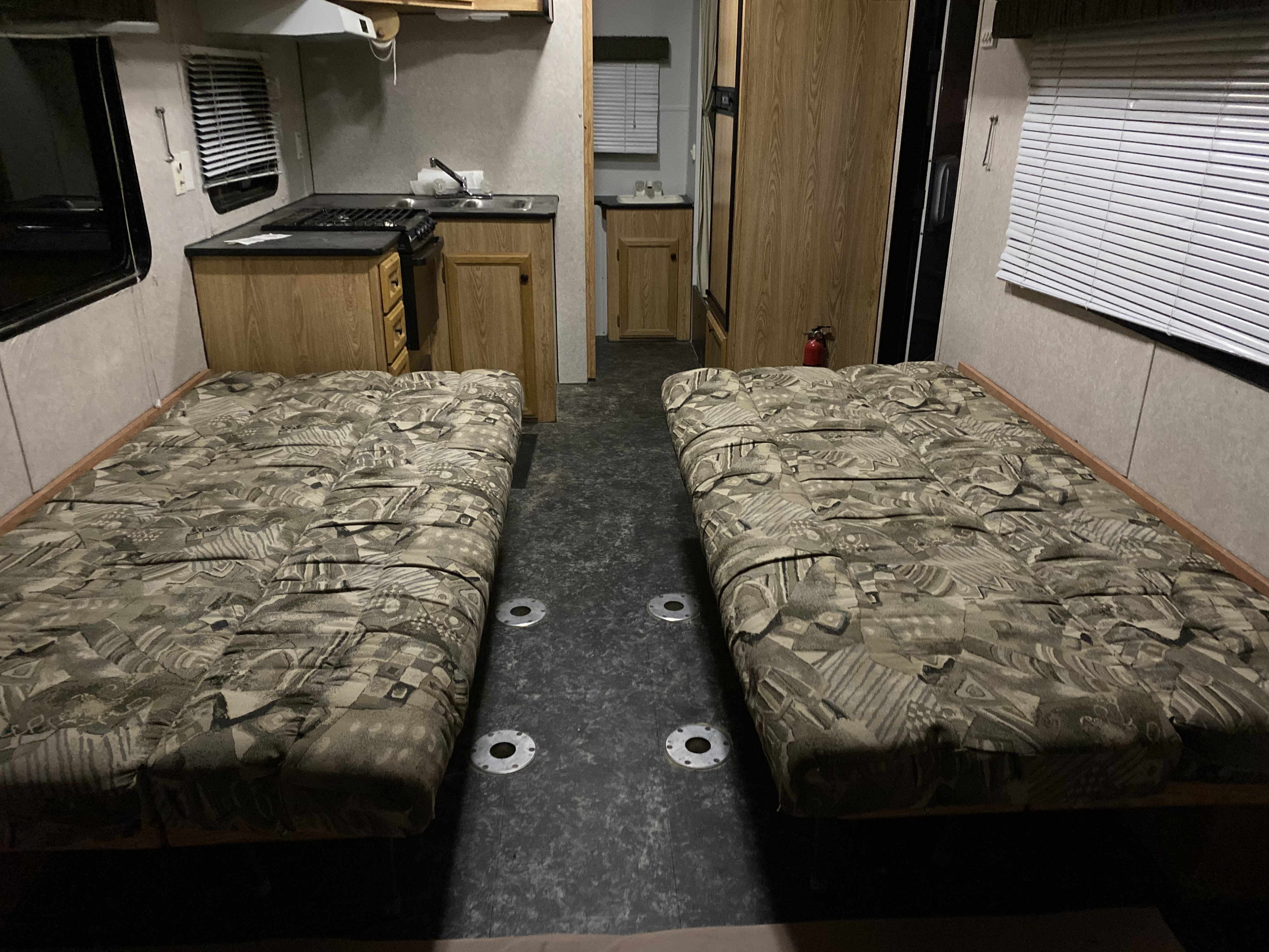 RV rental interior with two beds, a compact kitchen (stove, sink, cabinets), and a small vanity. Practical for travel.. Carson Trailer Fun Runner 2007