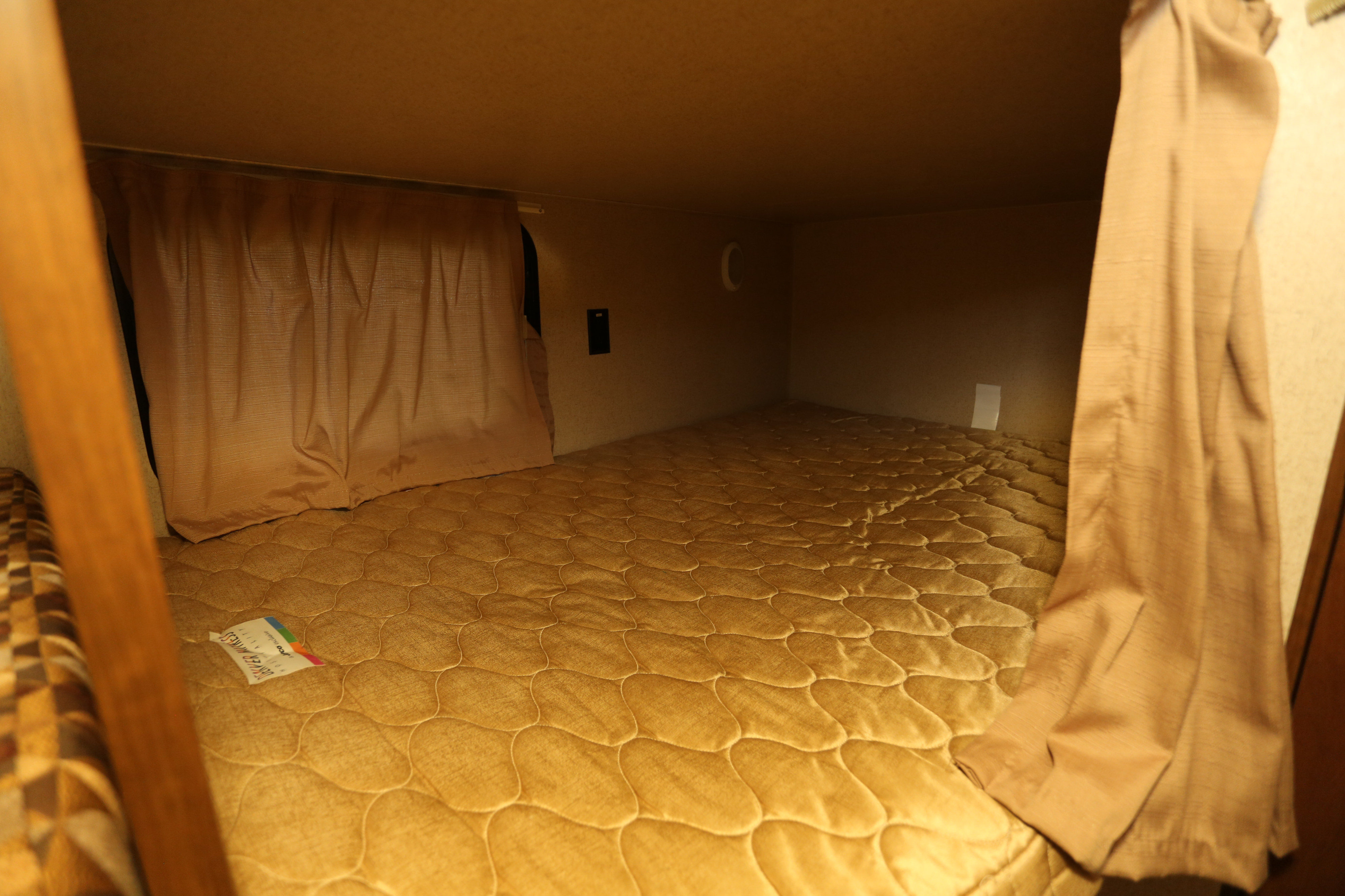 Cozy RV rental bunk bed featuring a quilted mattress, privacy curtains, and wall-mounted controls.. Jayco Jay Flight 2015