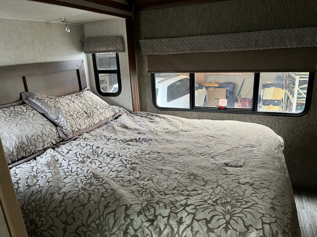 Comfortable RV rental bedroom with a large bed, patterned comforter, and windows offering a view outside. Ideal for travel.. Forest River Sunseeker 2018