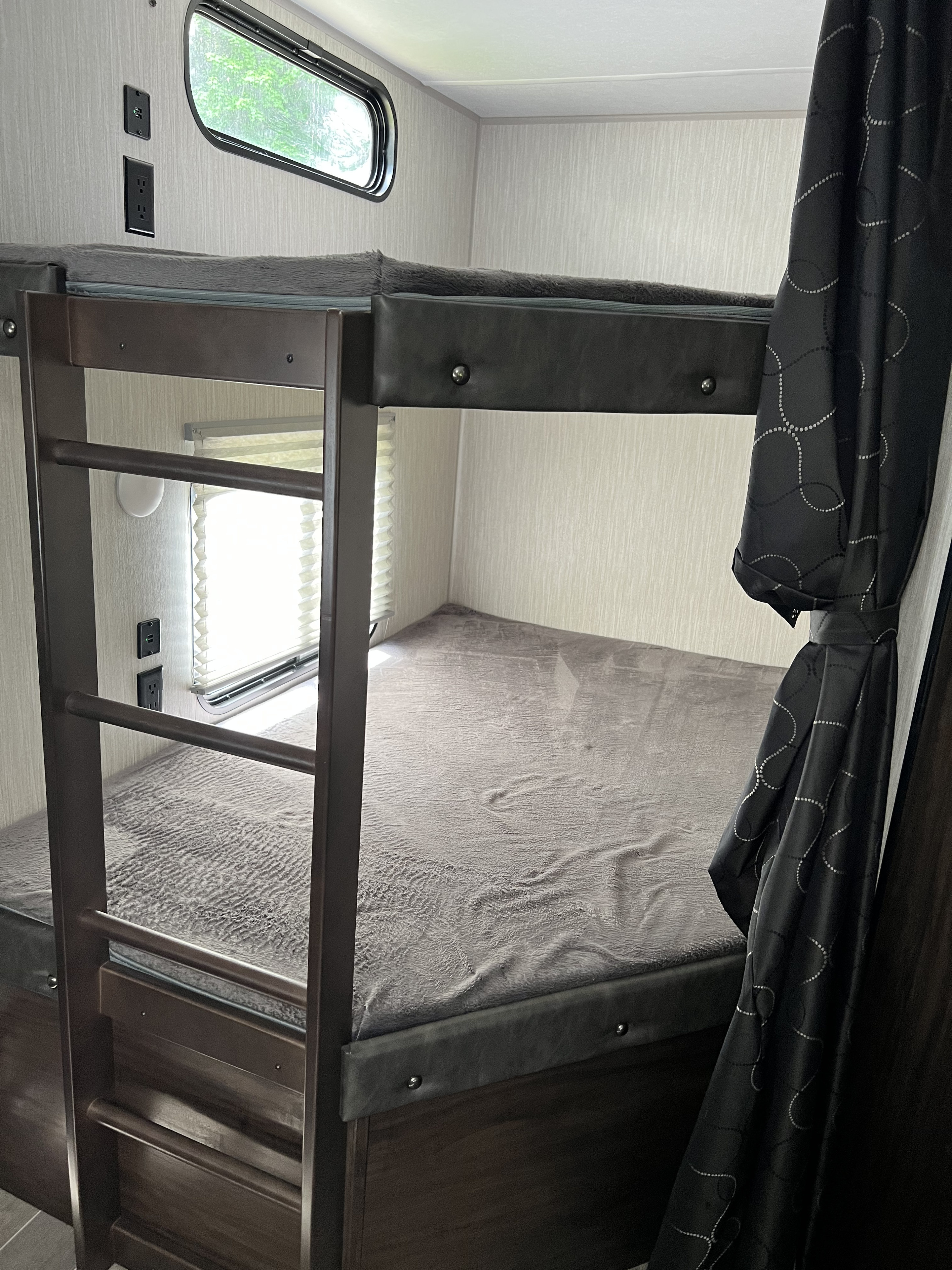 Cozy RV rental bunk beds with grey blankets, integrated ladder, window view, and convenient power outlets, perfect for family adventures.. Forest River Cherokee 2021